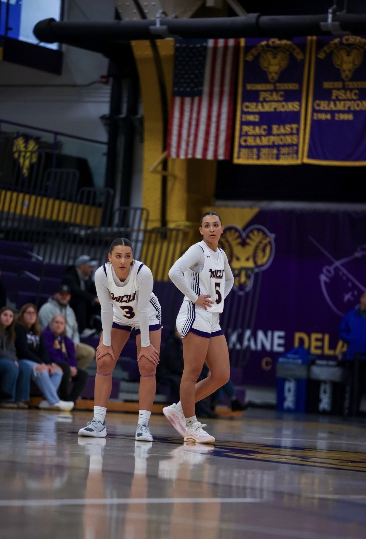 Two female basketball players in white uniforms numbered 3 and 5 stand on a hardwood court.