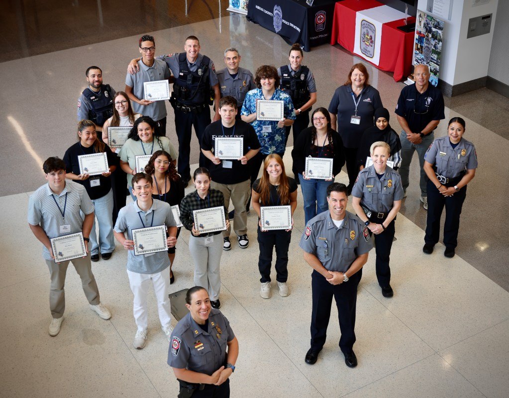 Group of students holding certificates posing with uniformed police officers in a building lobby.