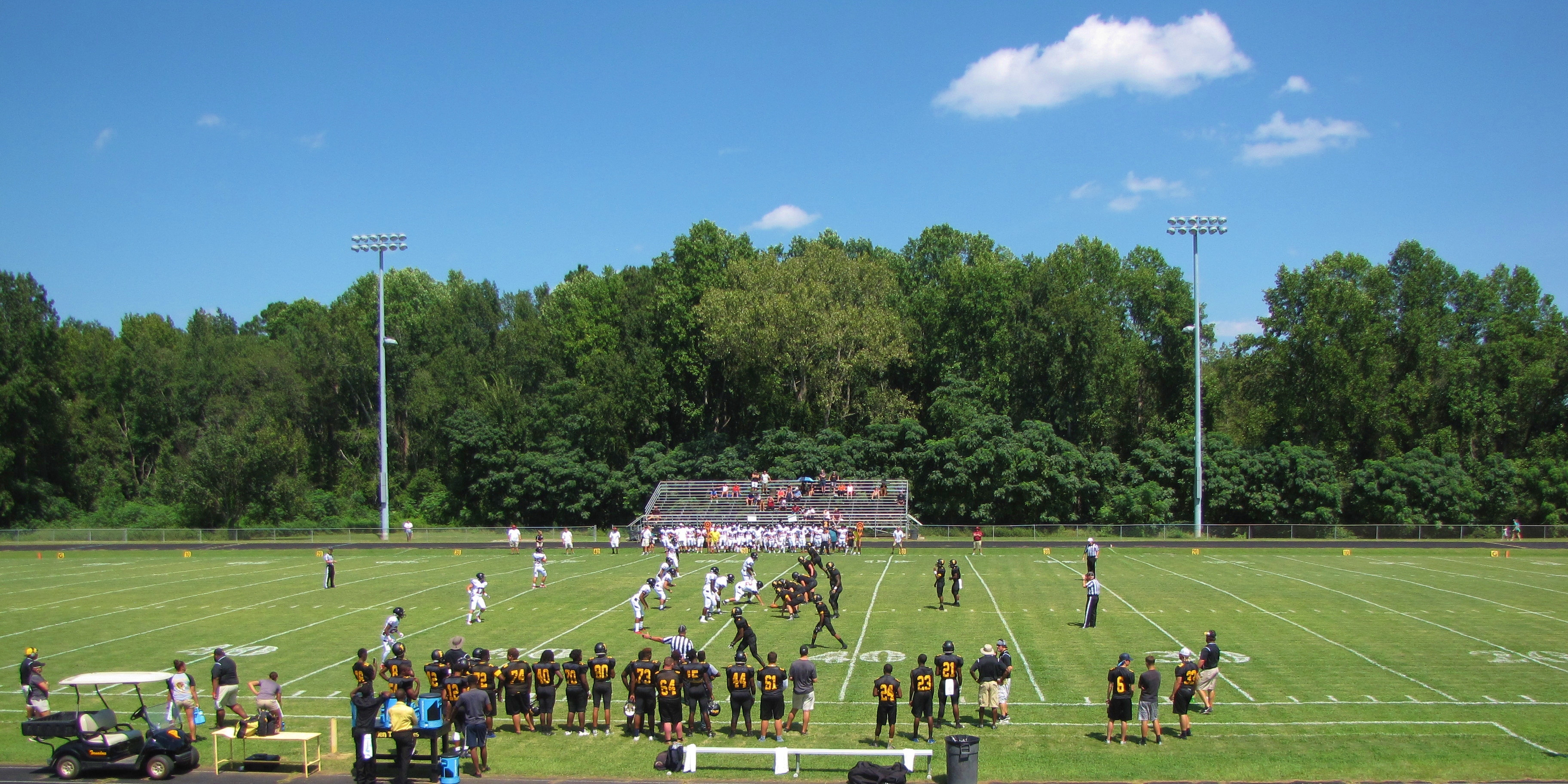 Wide view of a high school football game on a grass field with players and sideline staff.