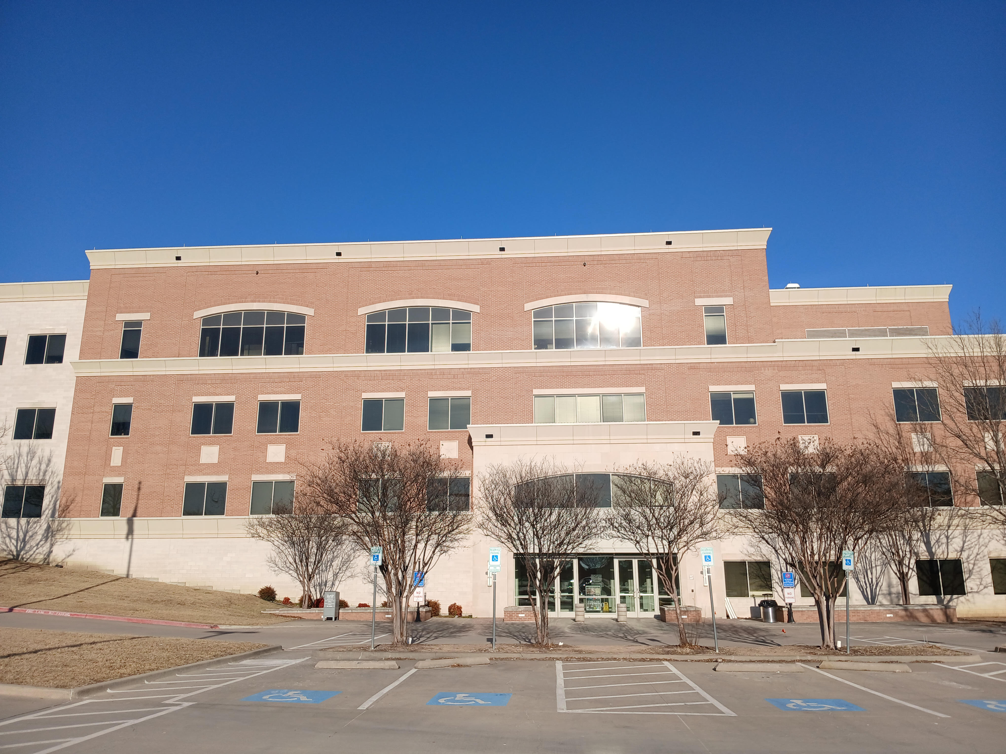 Multi-story brick government building with arched windows, bare trees, and accessible parking spaces.