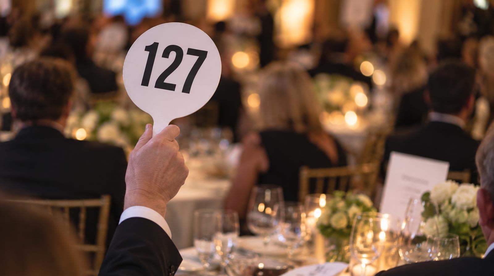 A numbered auction paddle raised above an elegantly set gala table.