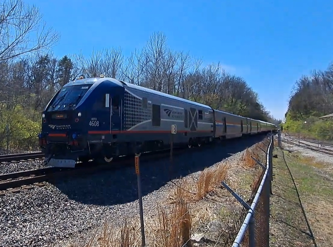 Amtrak passenger train traveling along a double-track rail line through a wooded area.