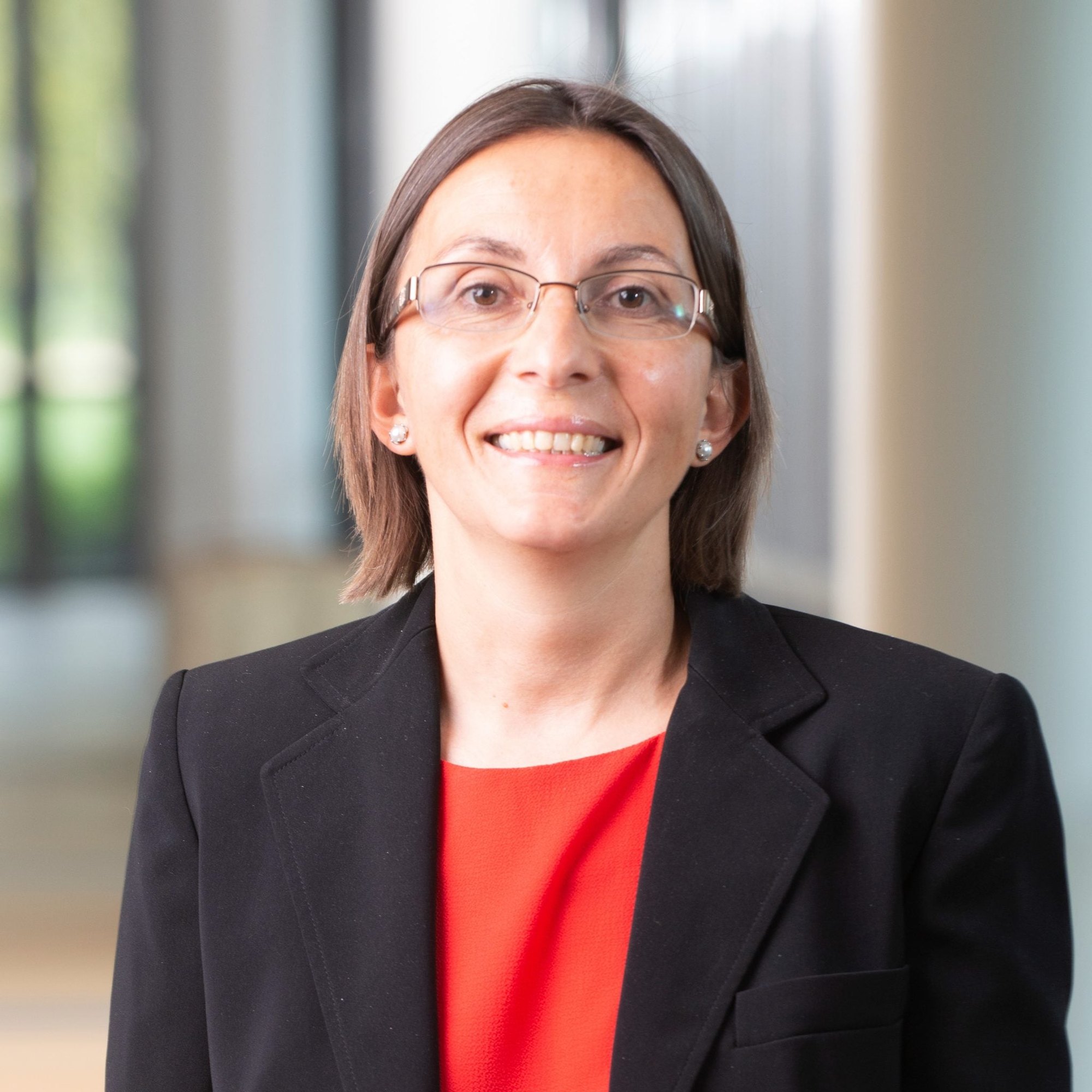 Woman in black blazer and red top smiling in a professional portrait.