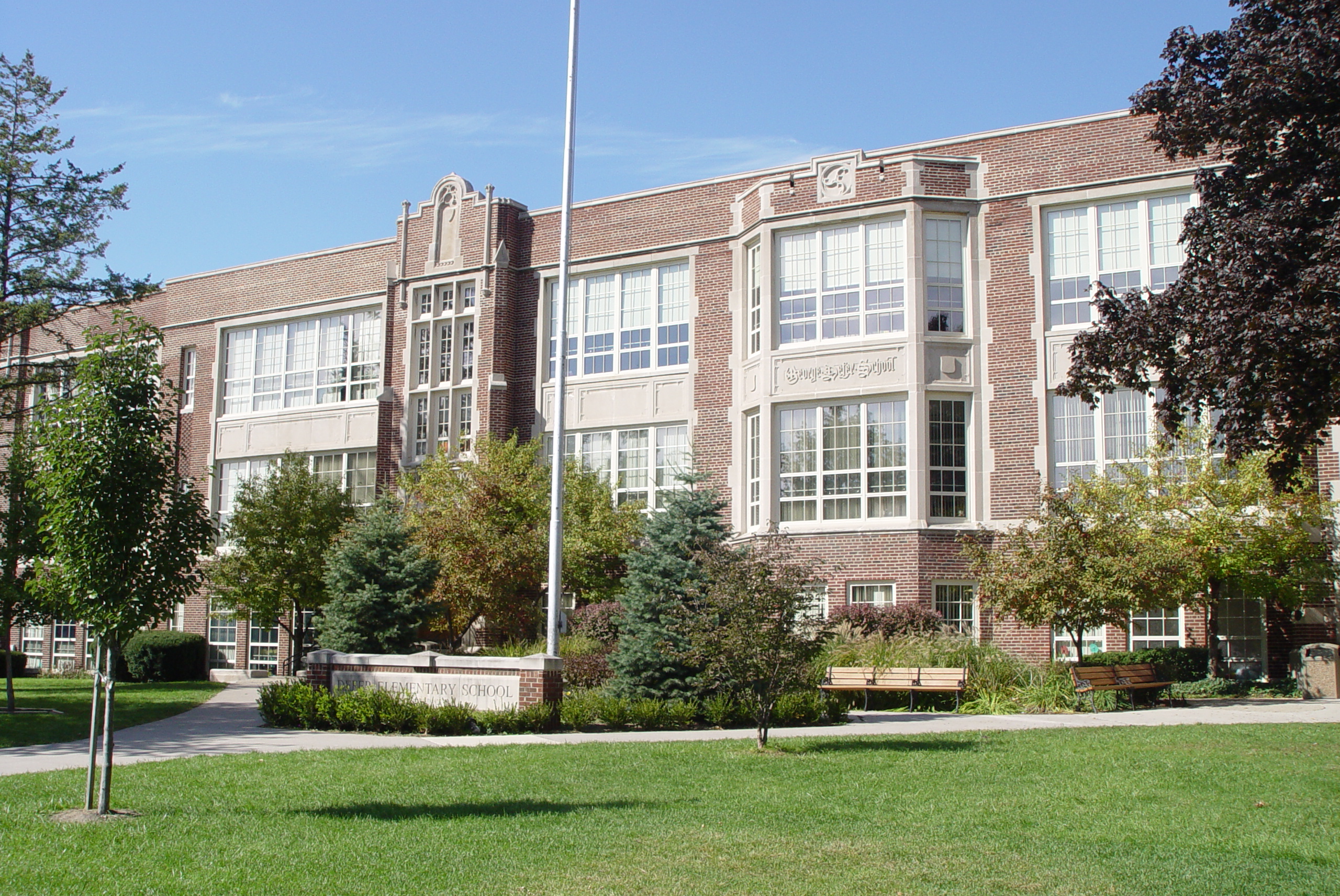 Multi-story red brick school building with flagpole and landscaped front lawn.