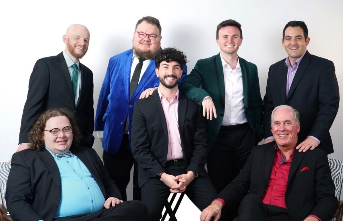 Seven adults in formal attire pose together in two rows for a group photo.