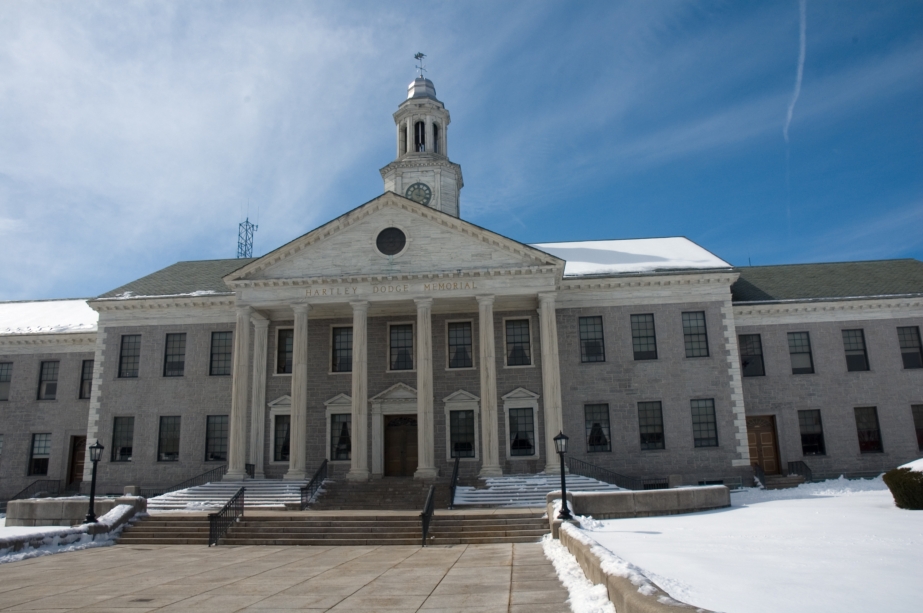 Neoclassical stone government building with white columns, clock tower, and snow-covered grounds.