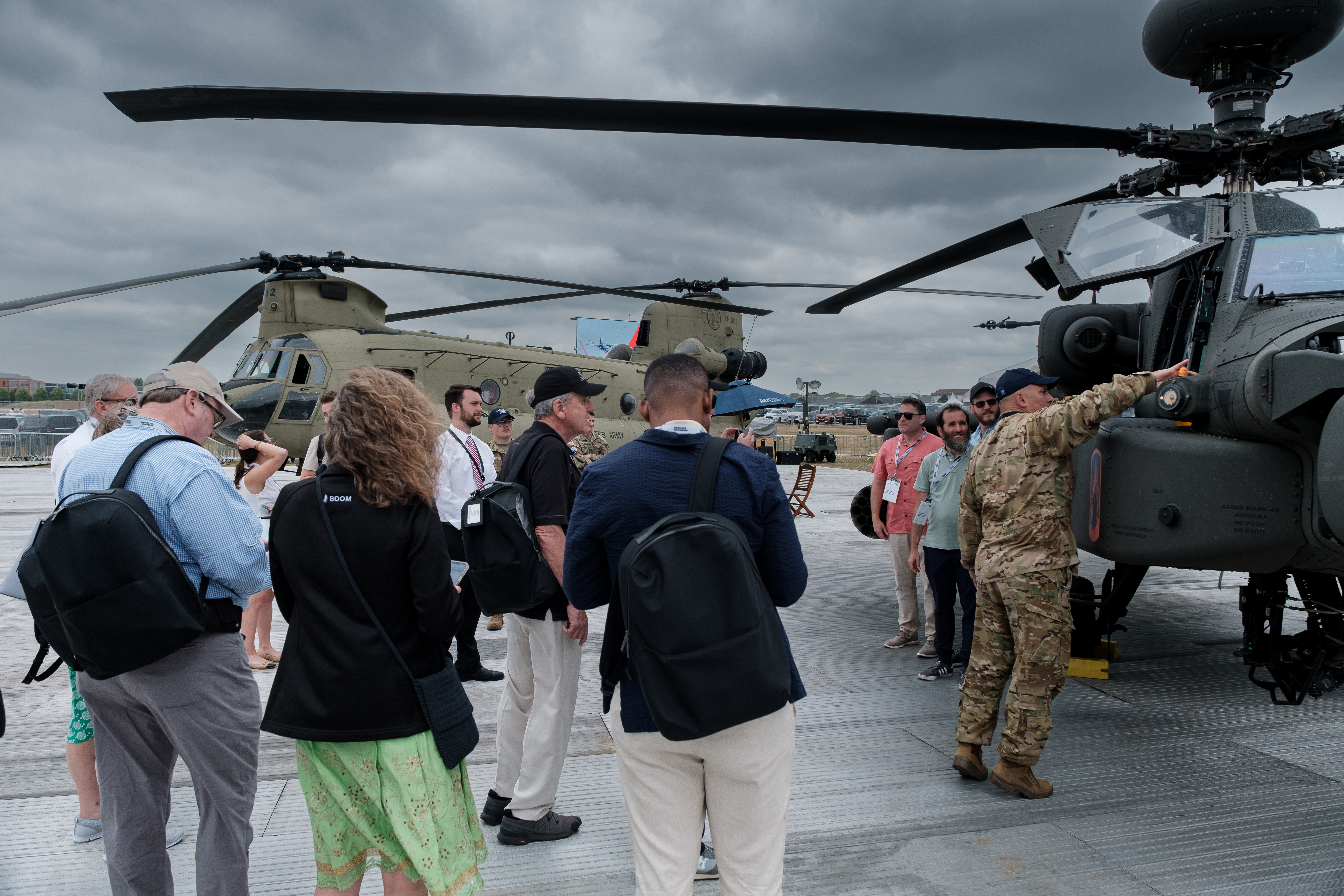 Civilians and a soldier examine a military helicopter on an airshow tarmac outdoors.