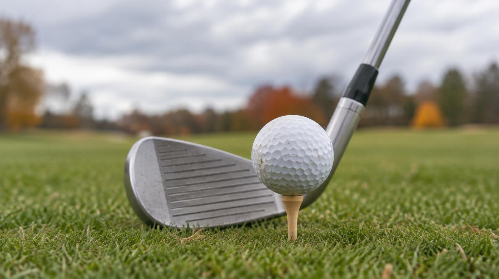 A golf ball on a wooden tee in green grass with a club head positioned behind it.