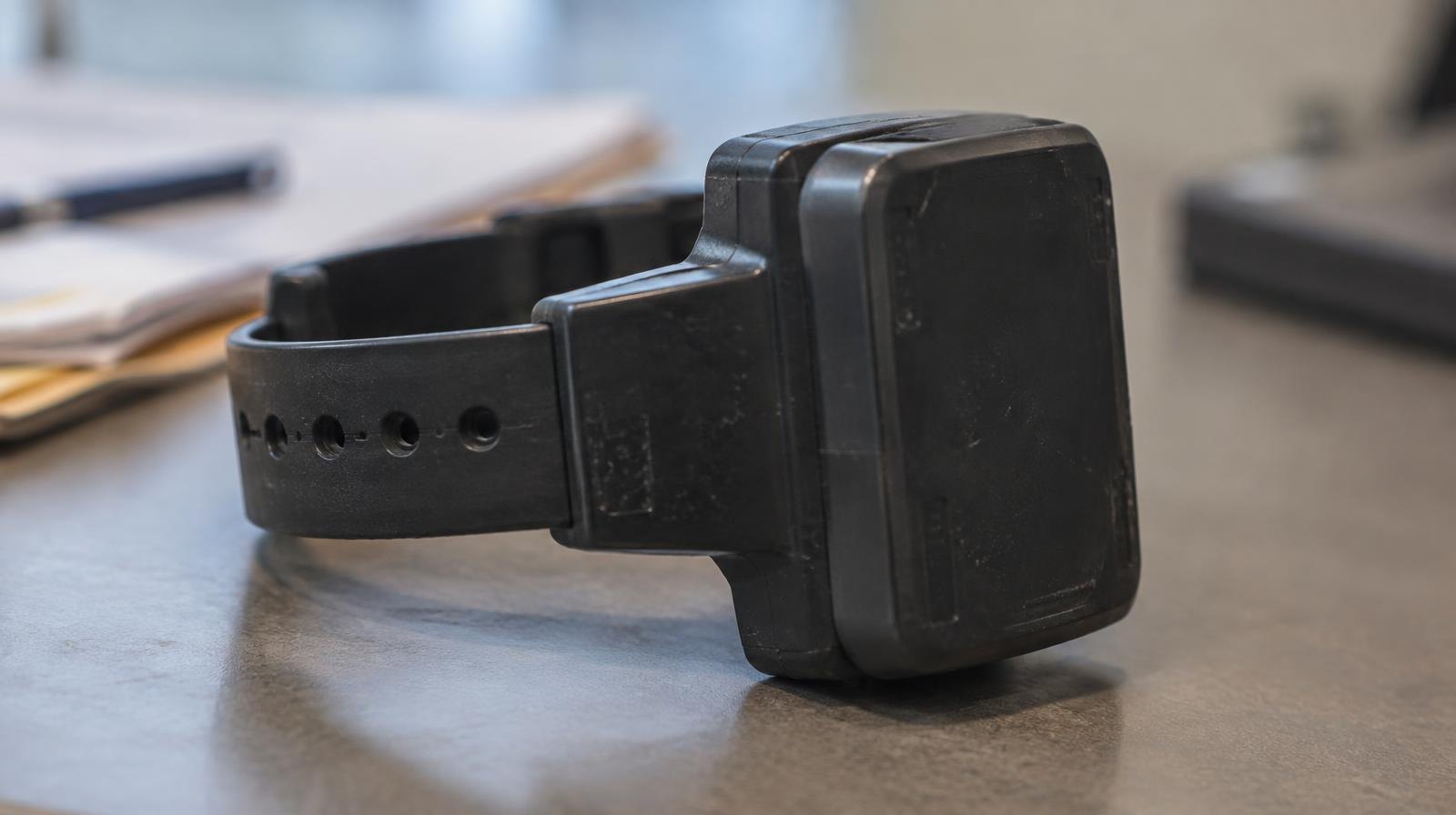 GPS electronic monitoring ankle bracelet with strap and tracking unit on a plain surface.