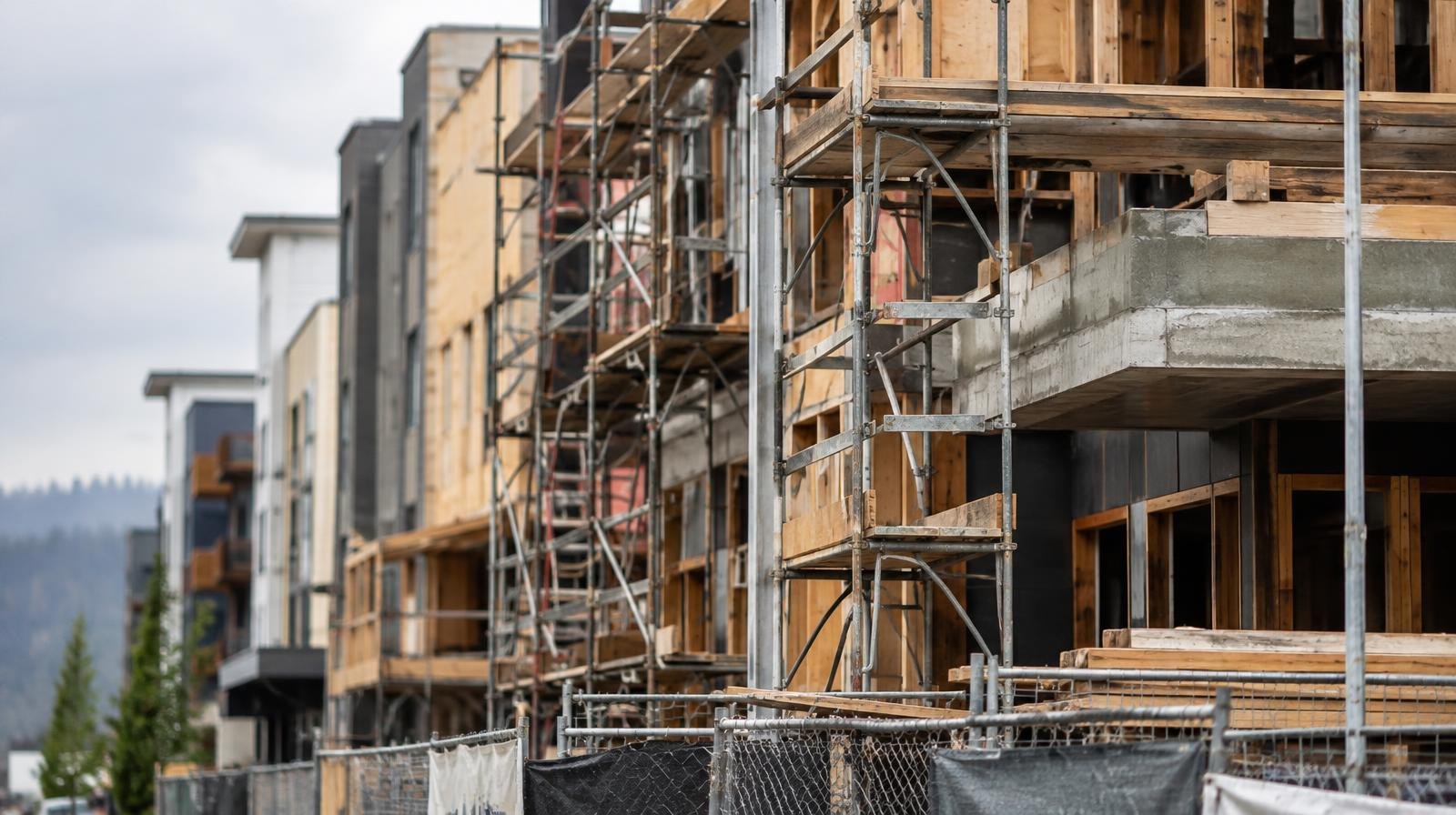 Row of urban mixed-use buildings under construction with scaffolding on a cloudy day.