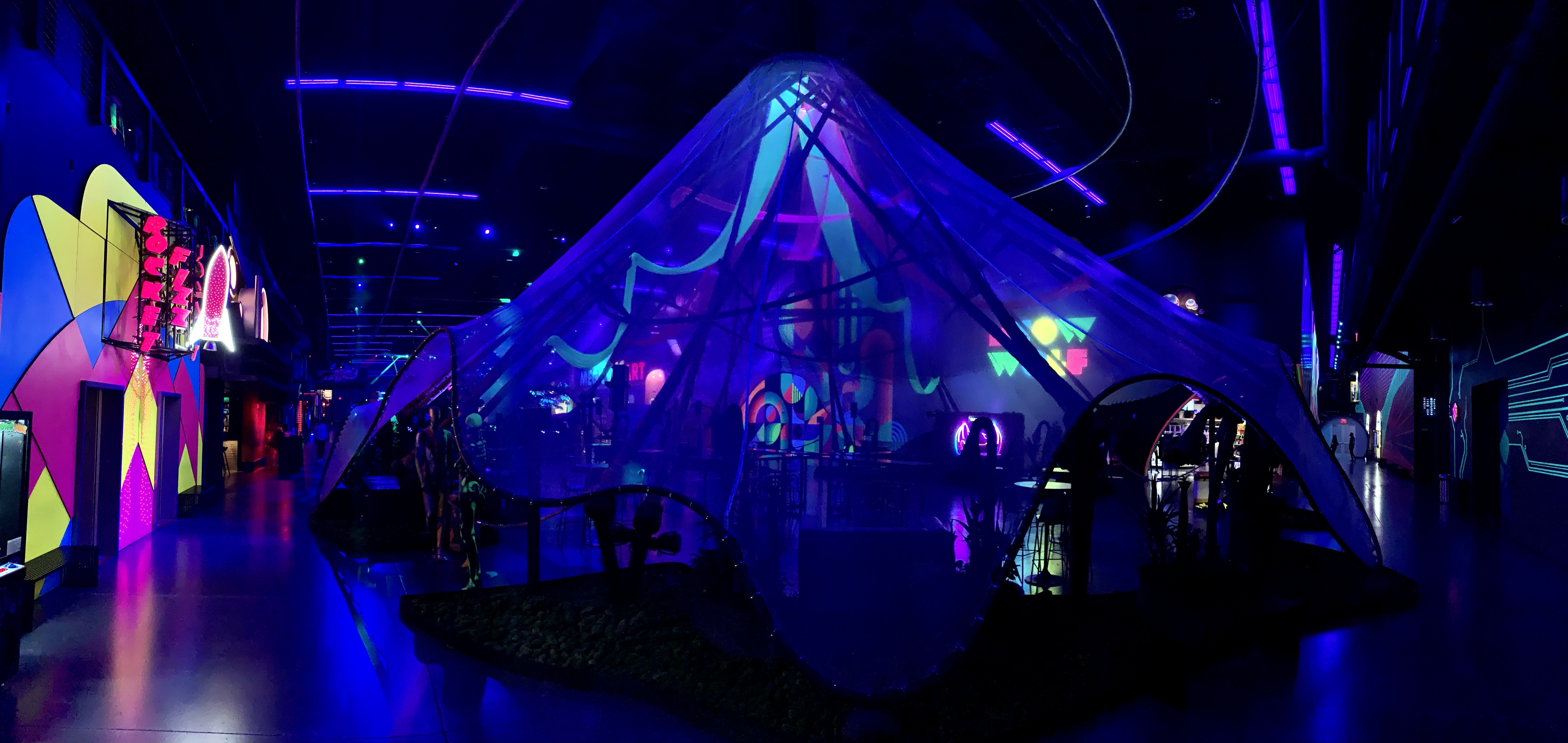 Darkened entertainment venue interior with blue and purple lighting and a large pyramid-shaped structure.