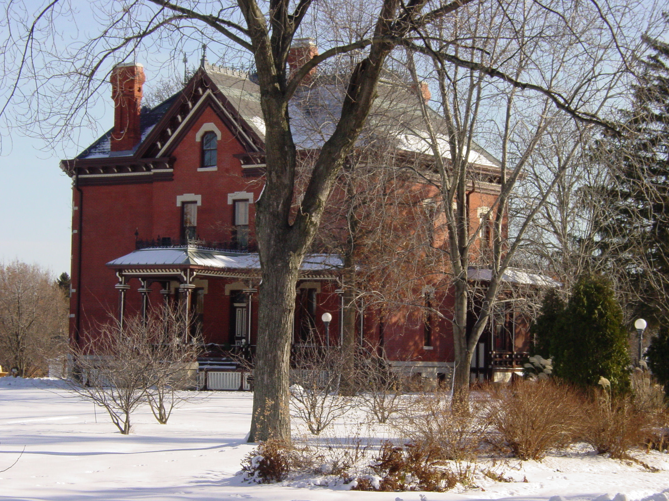 Red-brick Victorian mansion surrounded by bare trees and snow-covered grounds.