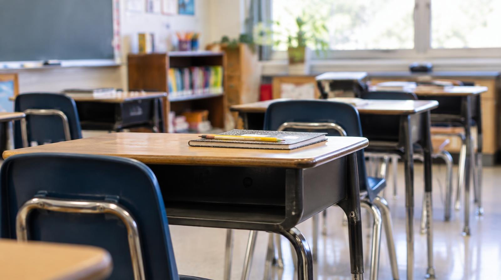 Rows of empty student desks in a bright school classroom.
