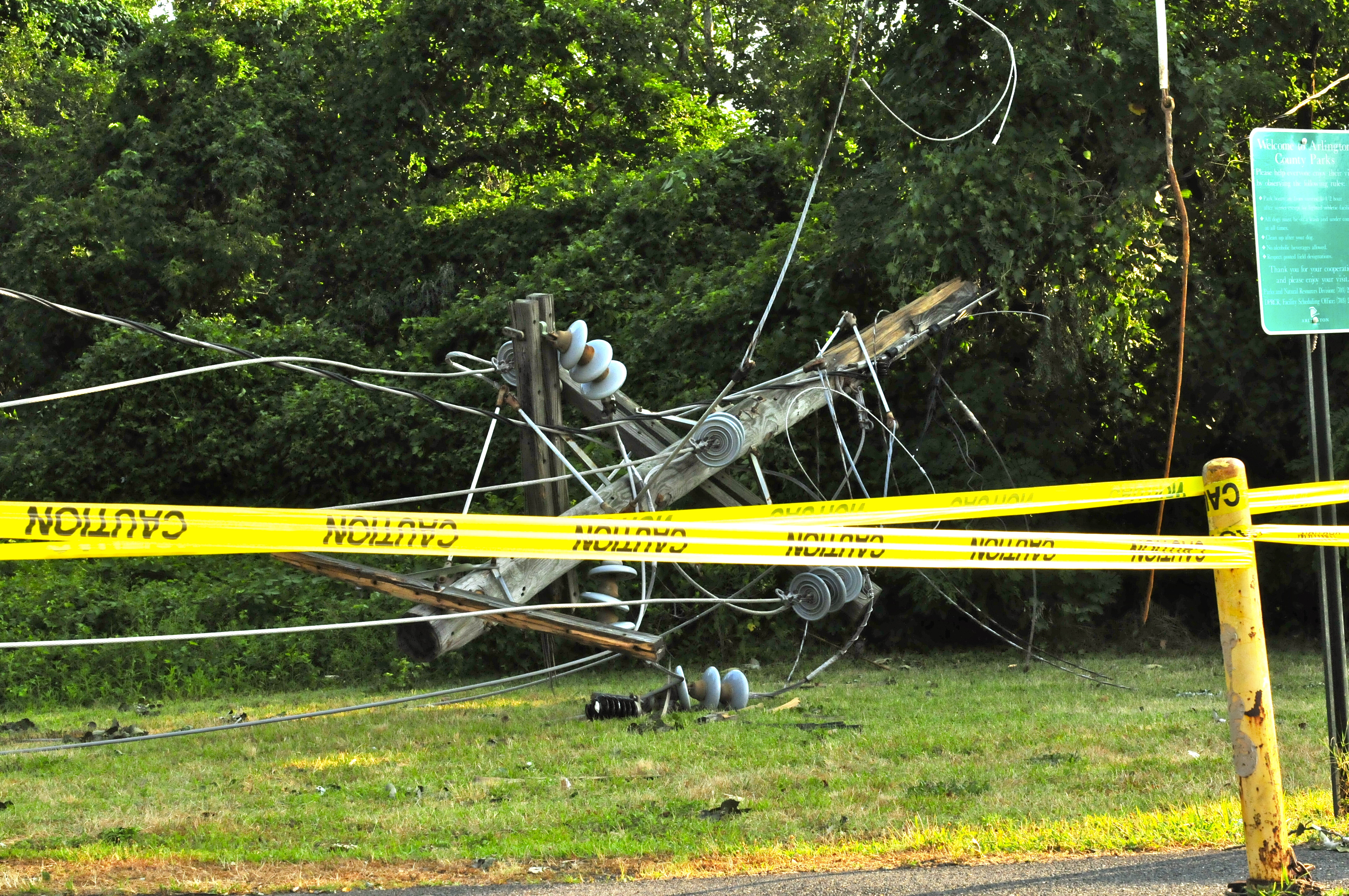 A fallen utility pole wrapped in yellow caution tape with downed wires on the ground.