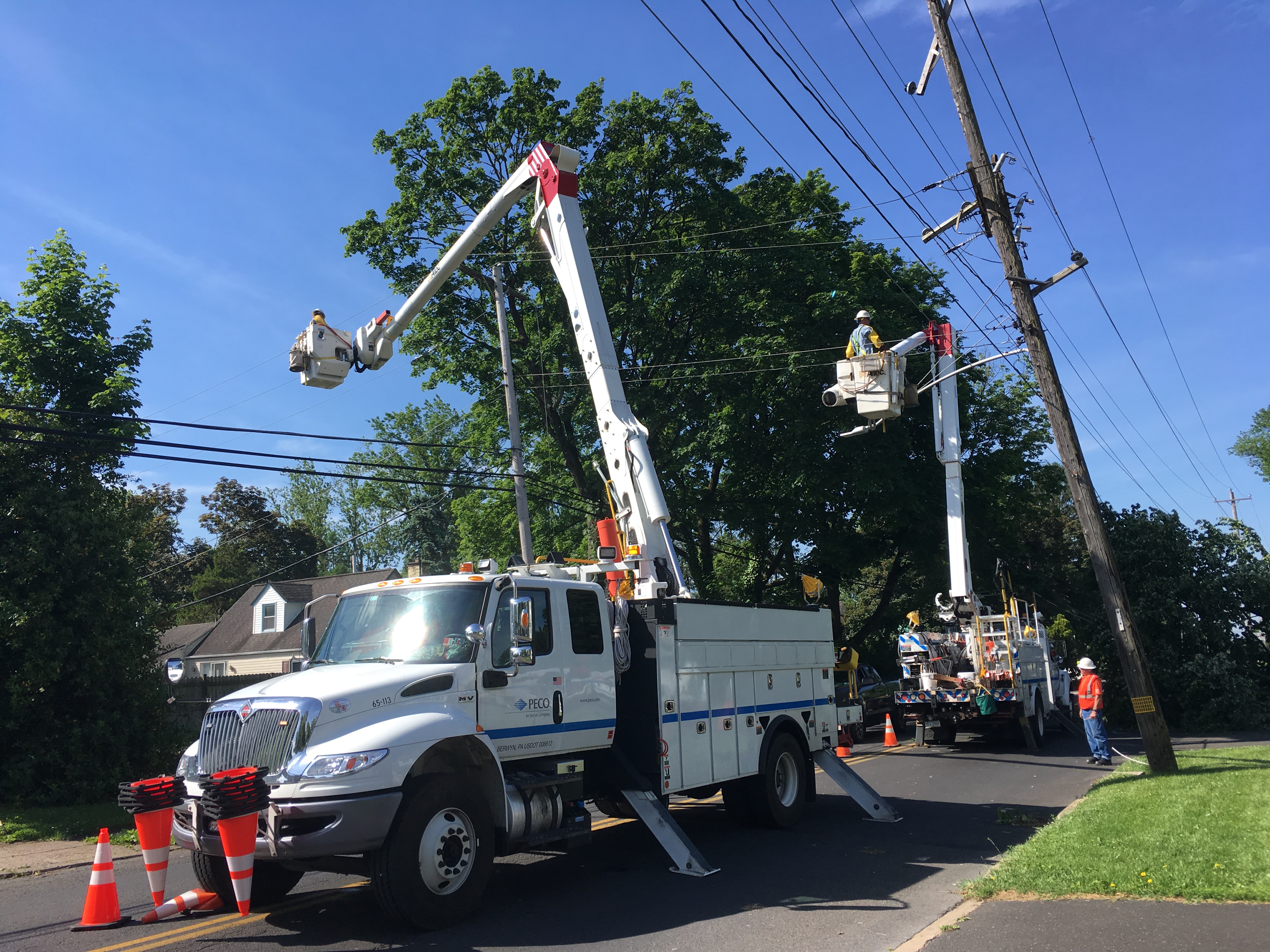 Two utility bucket trucks with workers repairing overhead power lines on a residential street