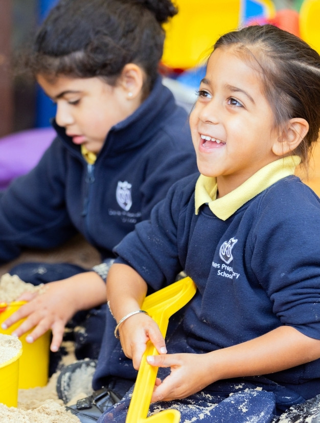 Two young children in school uniforms playing at an indoor sensory table
