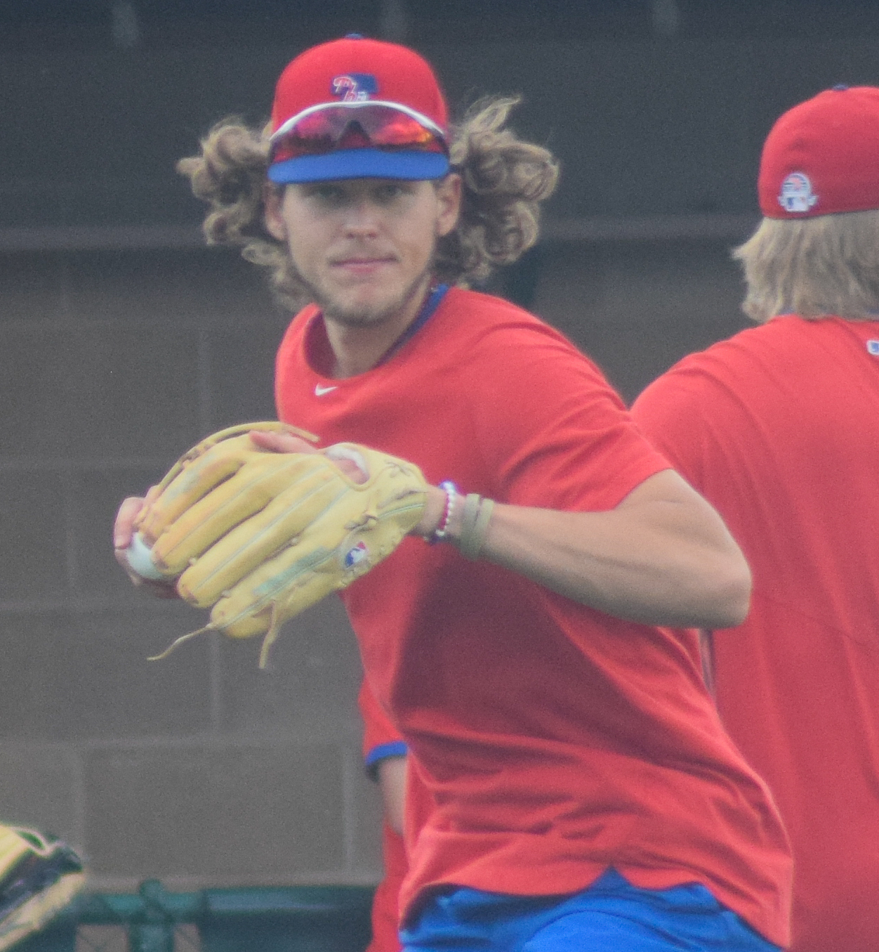 Baseball player in a red Phillies jersey and blue cap holding a tan glove.