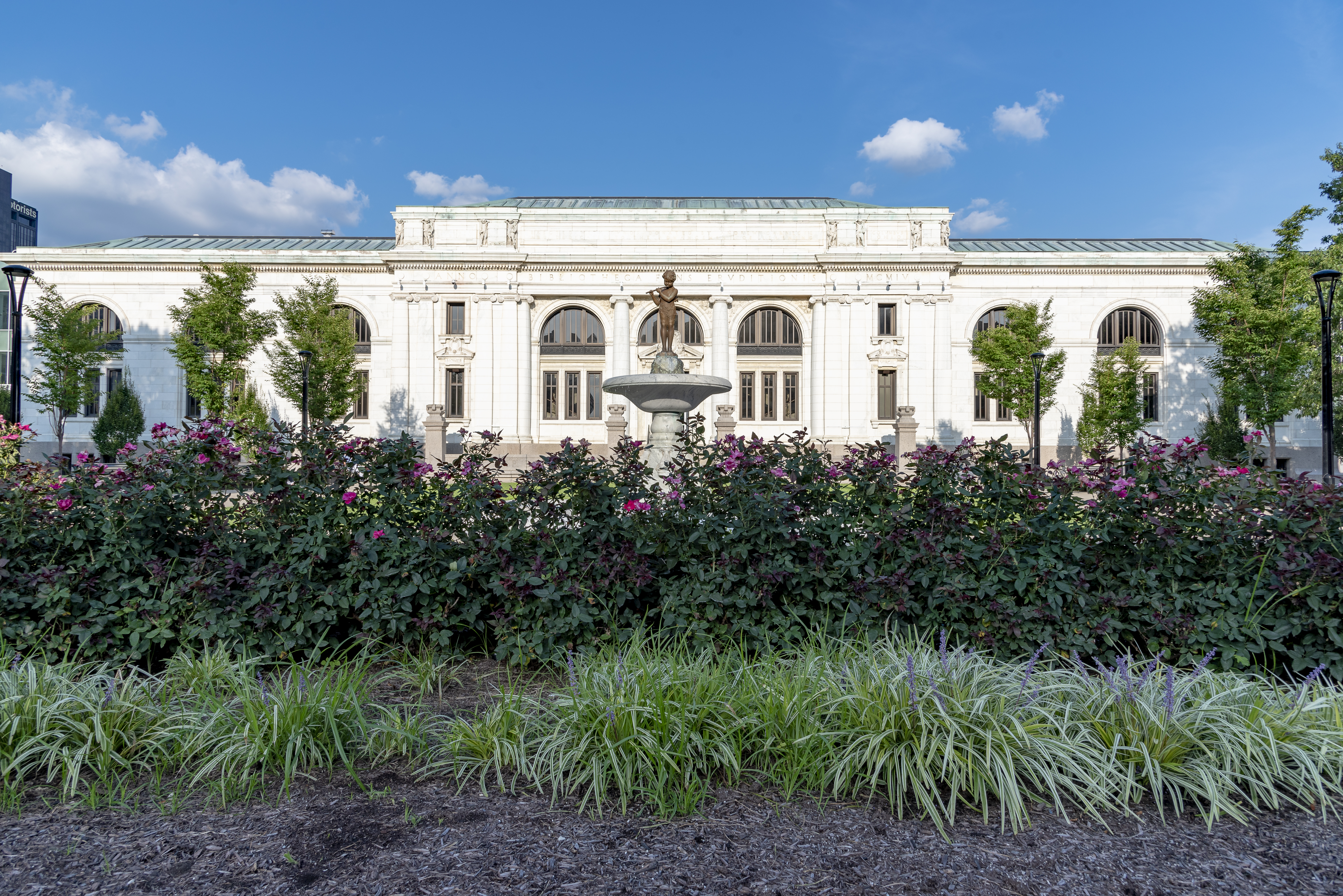 Neoclassical white library building with a decorative fountain in the foreground plaza.