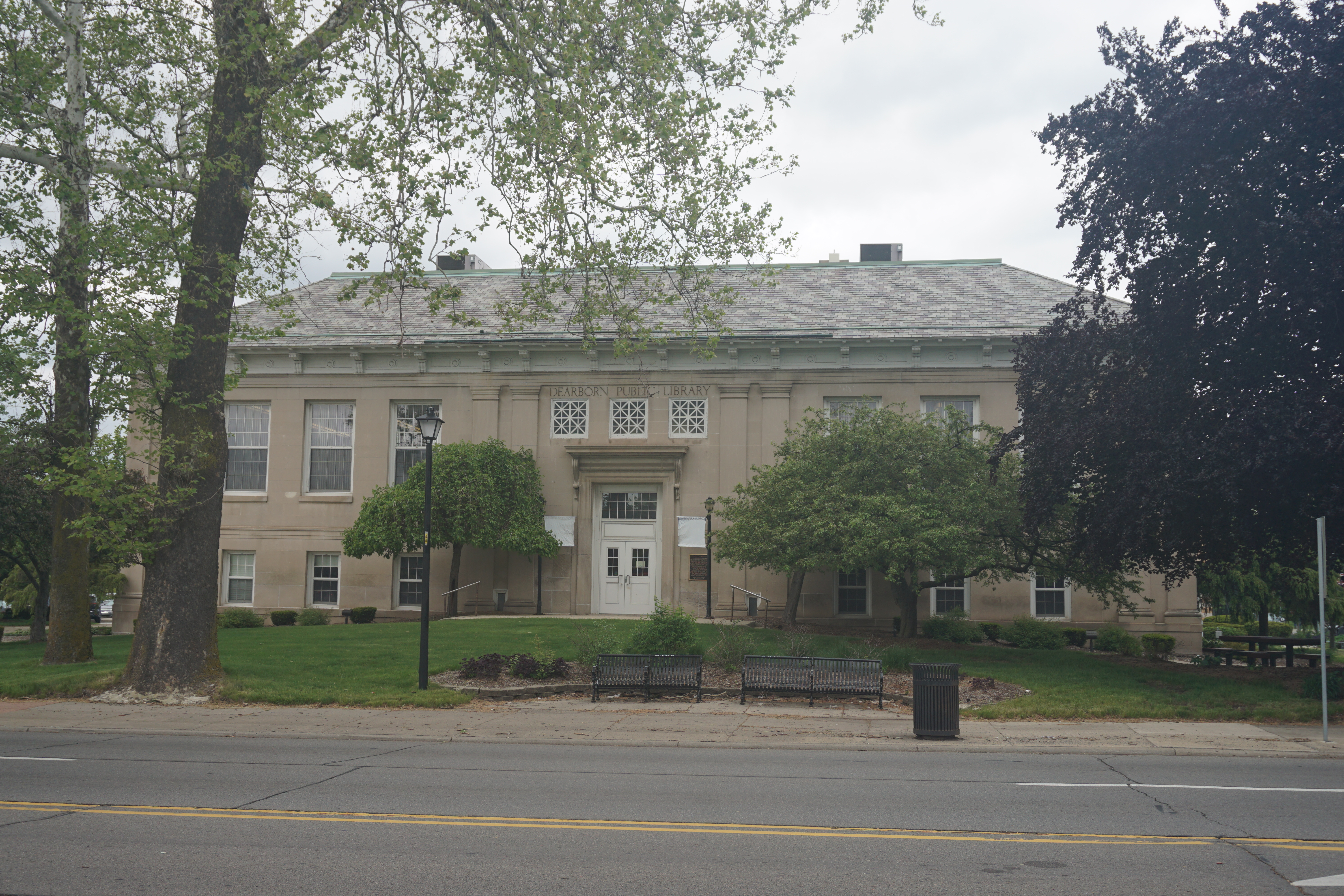 Two-story neoclassical library building with trees and a green lawn, viewed from across the street.