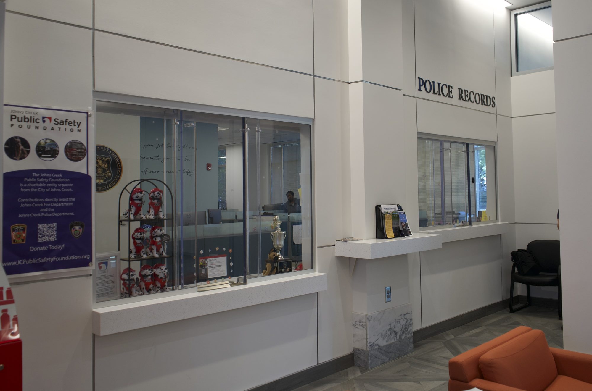 Interior lobby of a police records counter with service window and orange seating.