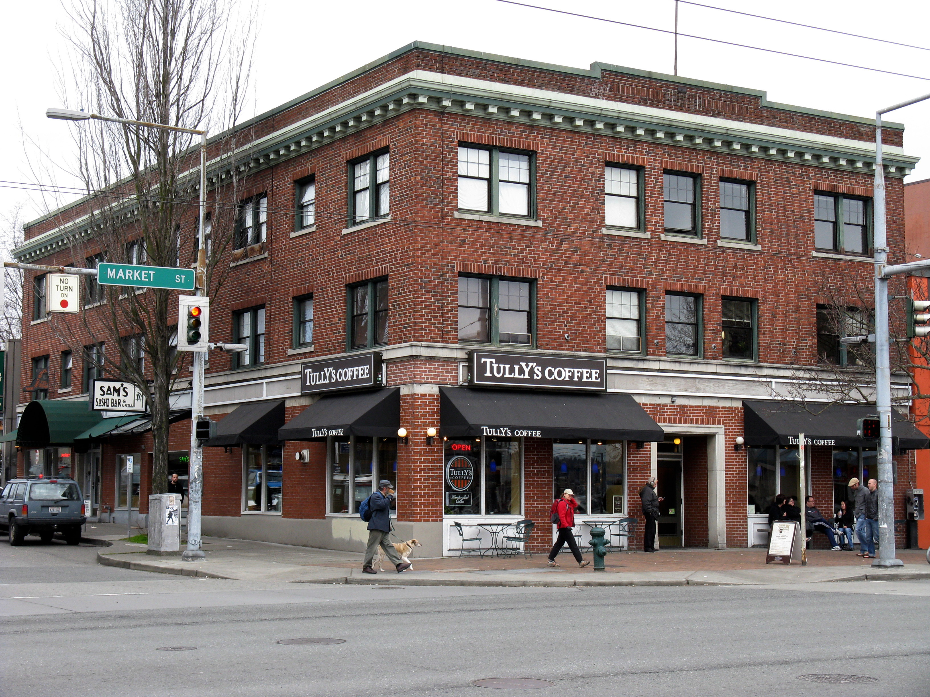 Three-story brick corner building on a commercial street with ground-floor storefronts and pedestrians.