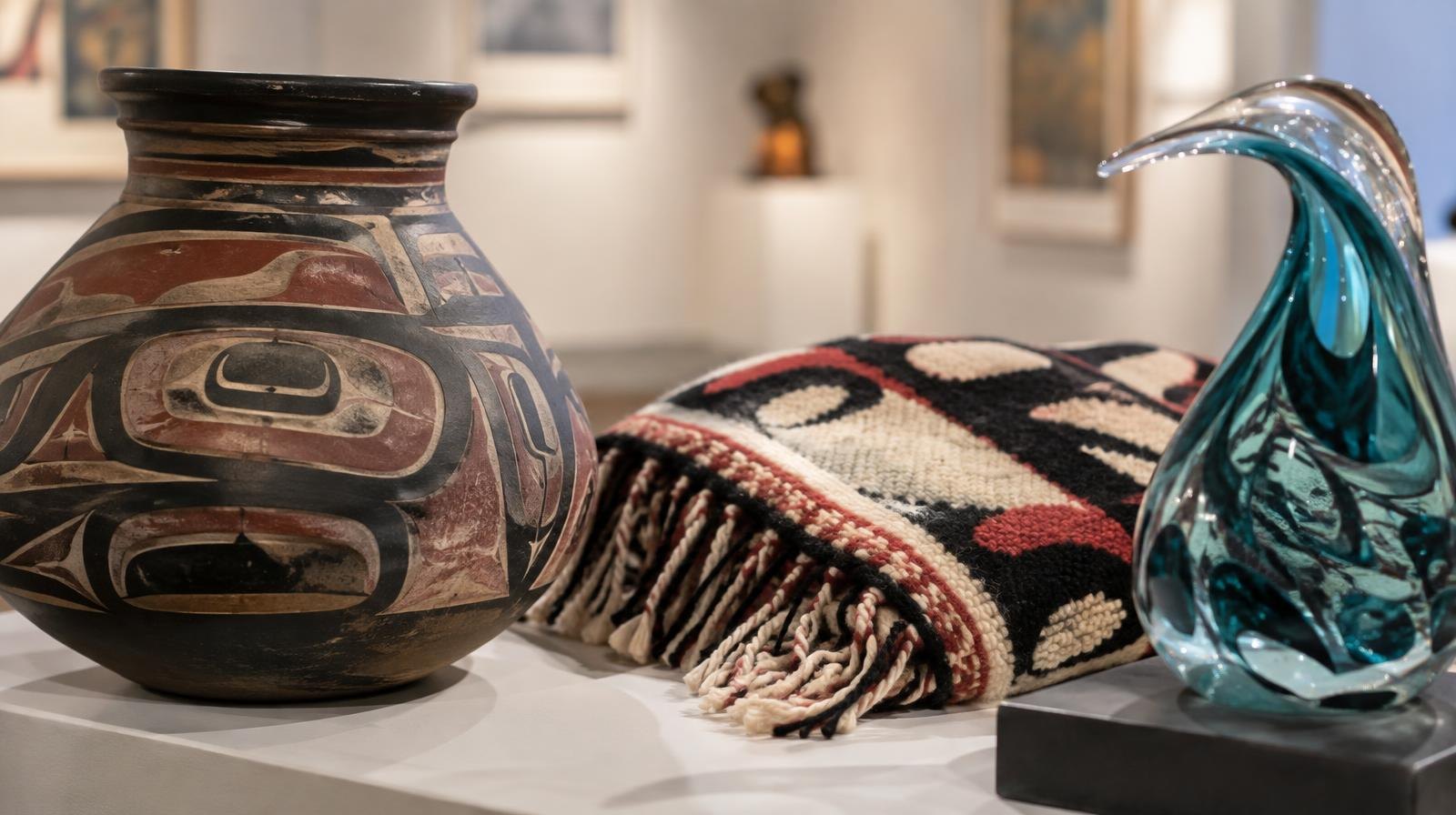 A ceramic vessel, woven textile, and glass sculpture arranged on a gallery surface.