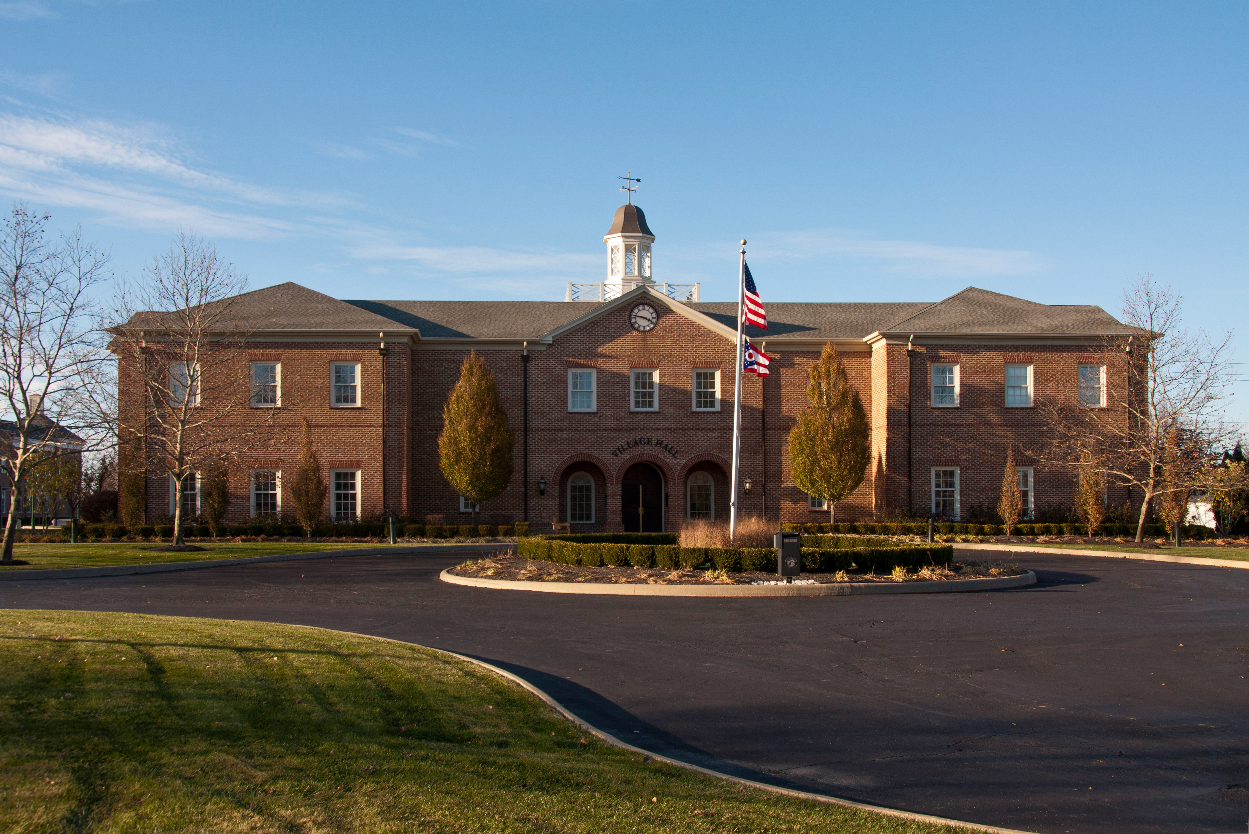 Two-story red brick city hall with white cupola and American flag out front.