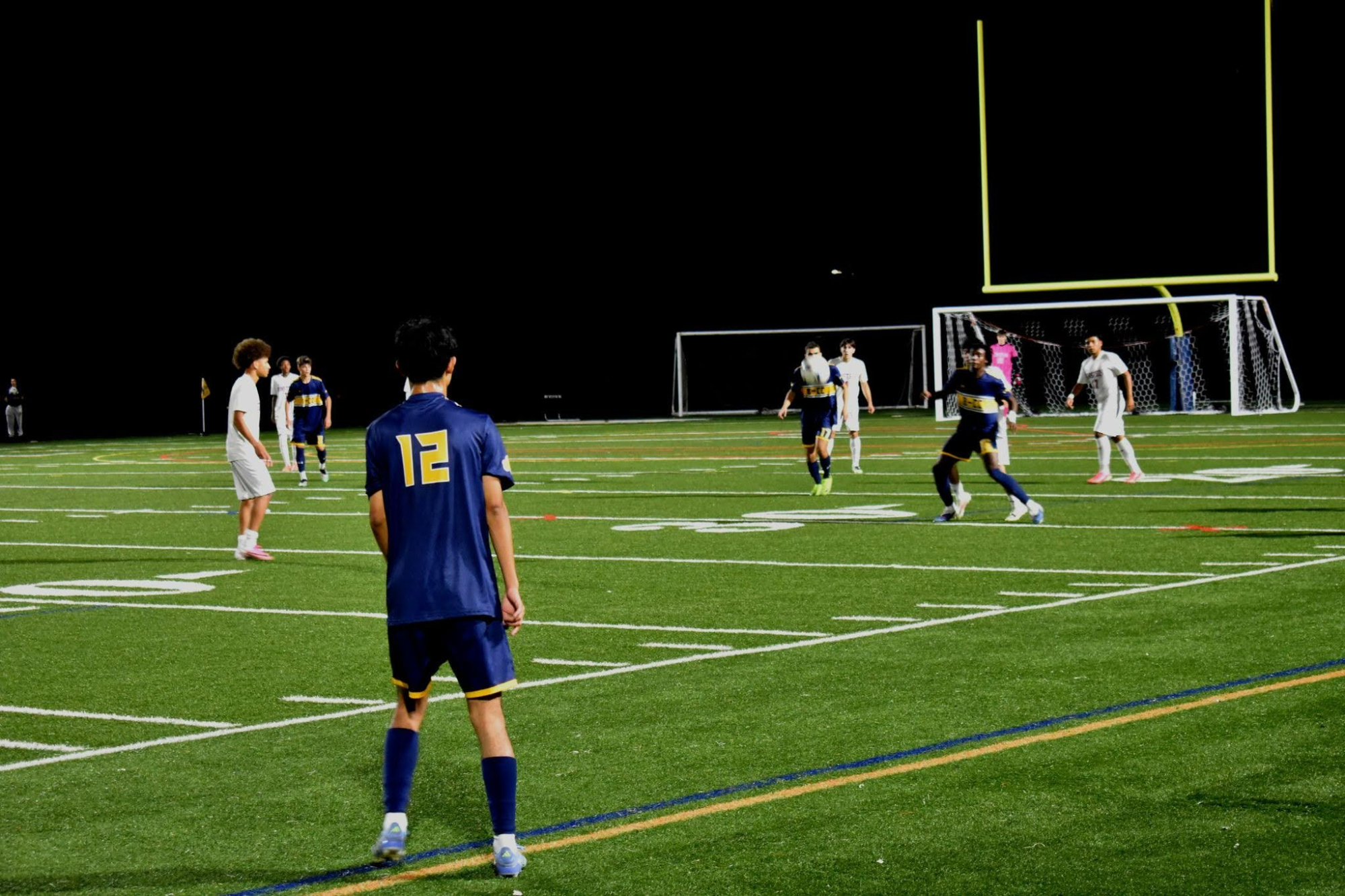 Soccer players in navy and gold uniforms on a turf field under stadium lights at night.