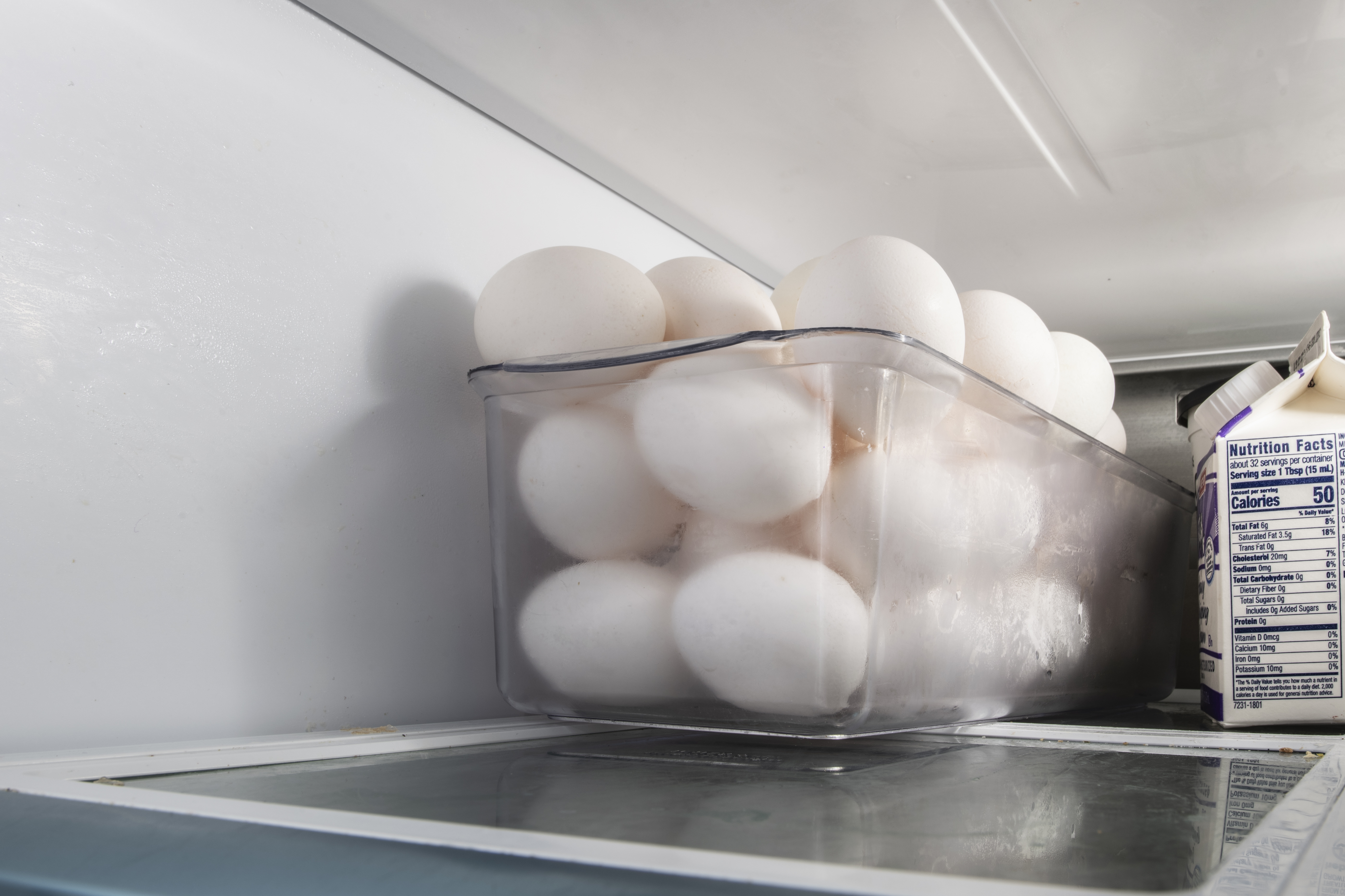 Raw white eggs in a clear plastic container on a refrigerator shelf.