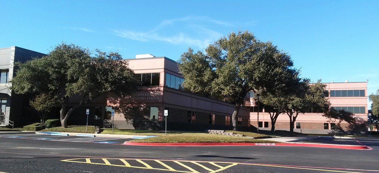 Multi-story brick and stucco school district building surrounded by trees under a blue sky.