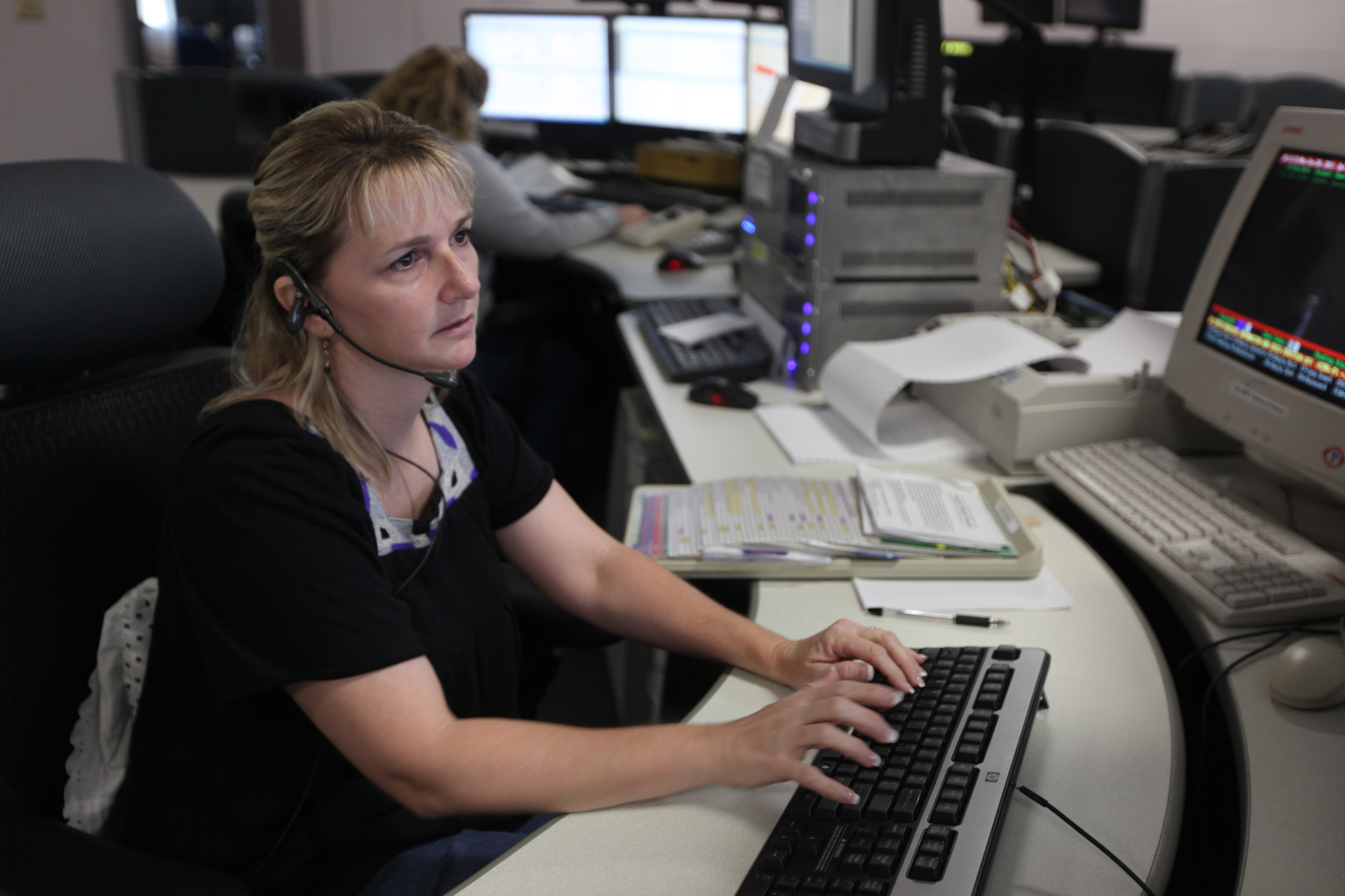 Dispatcher wearing a headset works at a multi-screen 911 console.