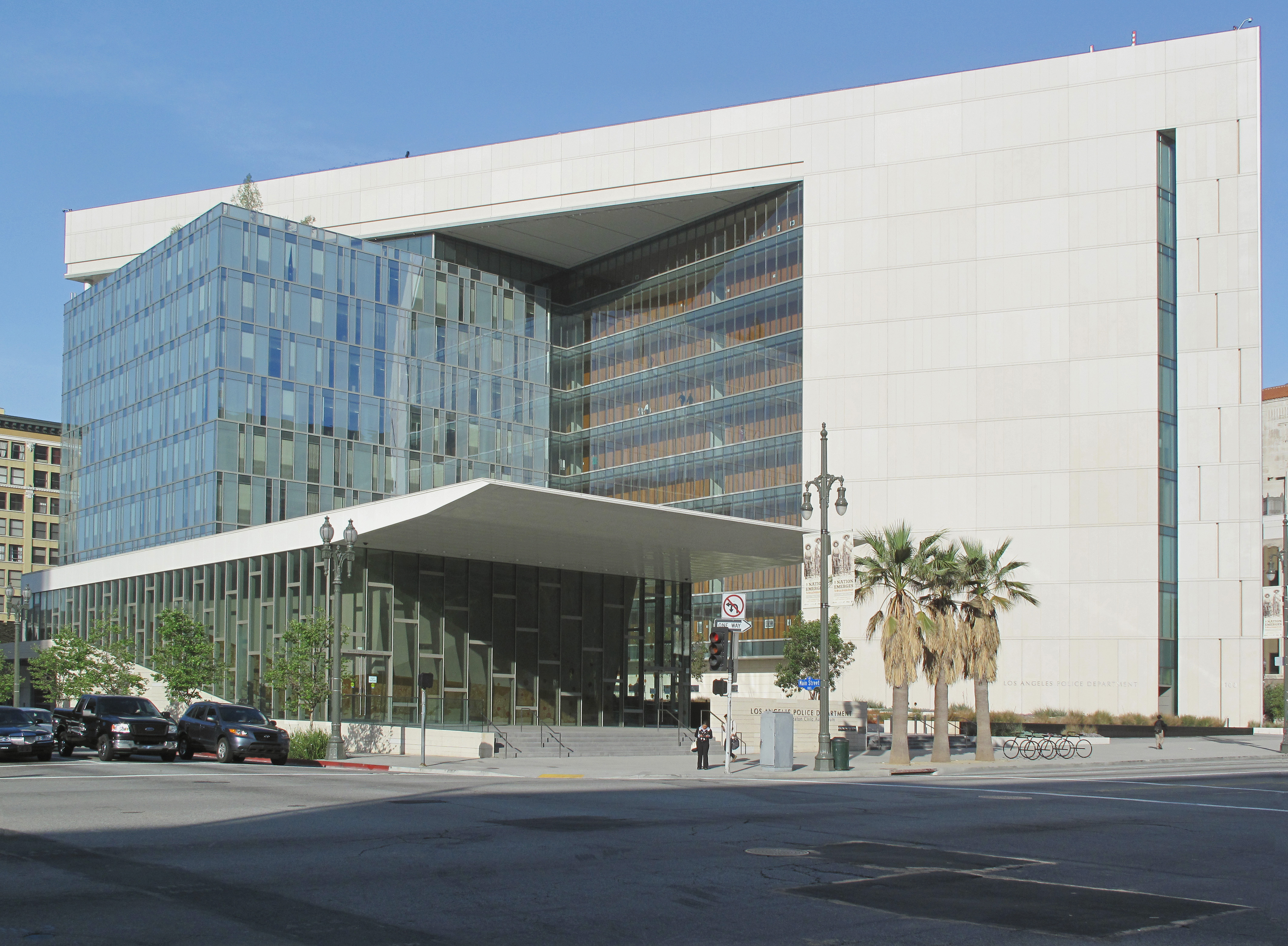Modern glass and stone LAPD headquarters building with palm trees outside.