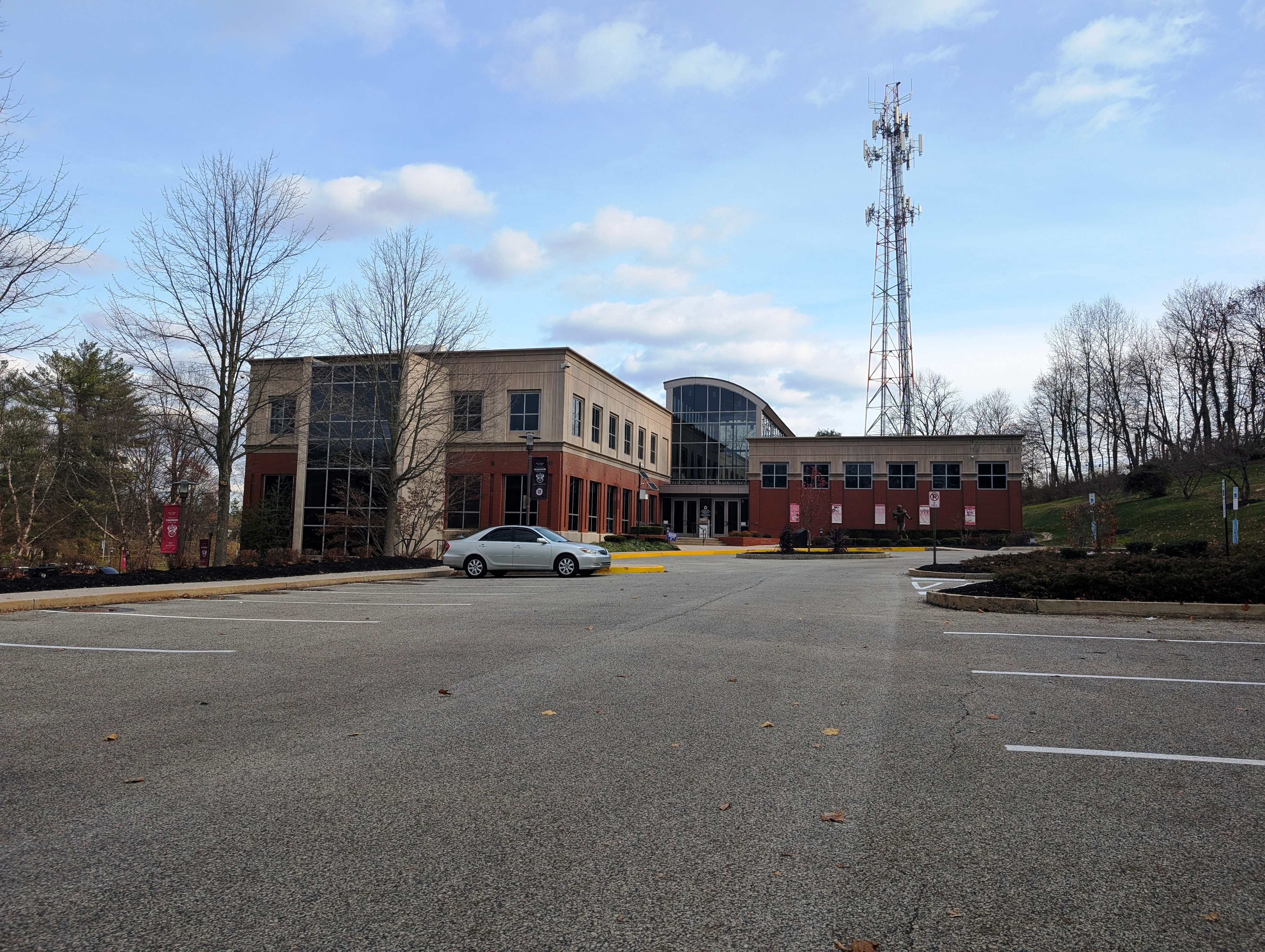 Two-story brick municipal building with large glass windows and a parking lot in front.