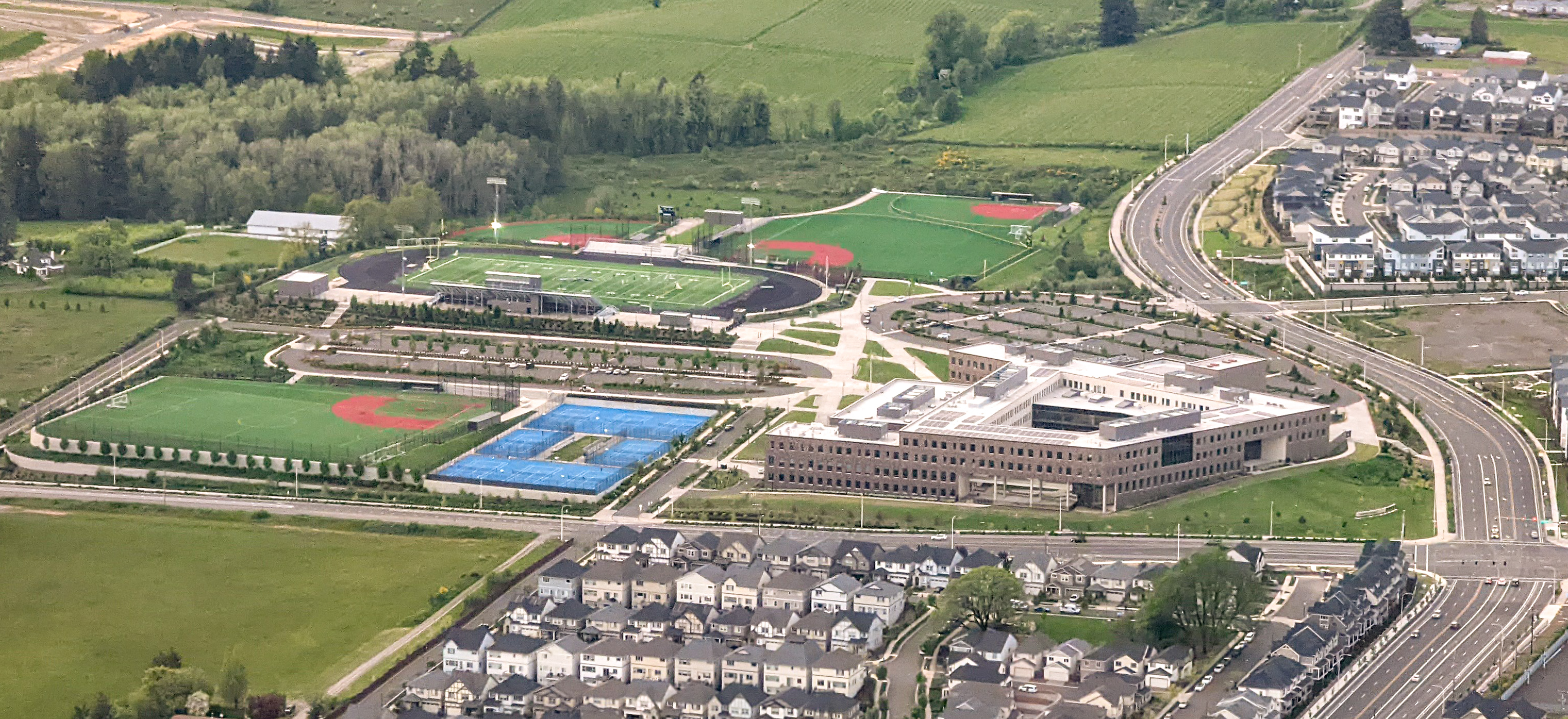 Aerial view of a school campus with a blue turf field and modern building.