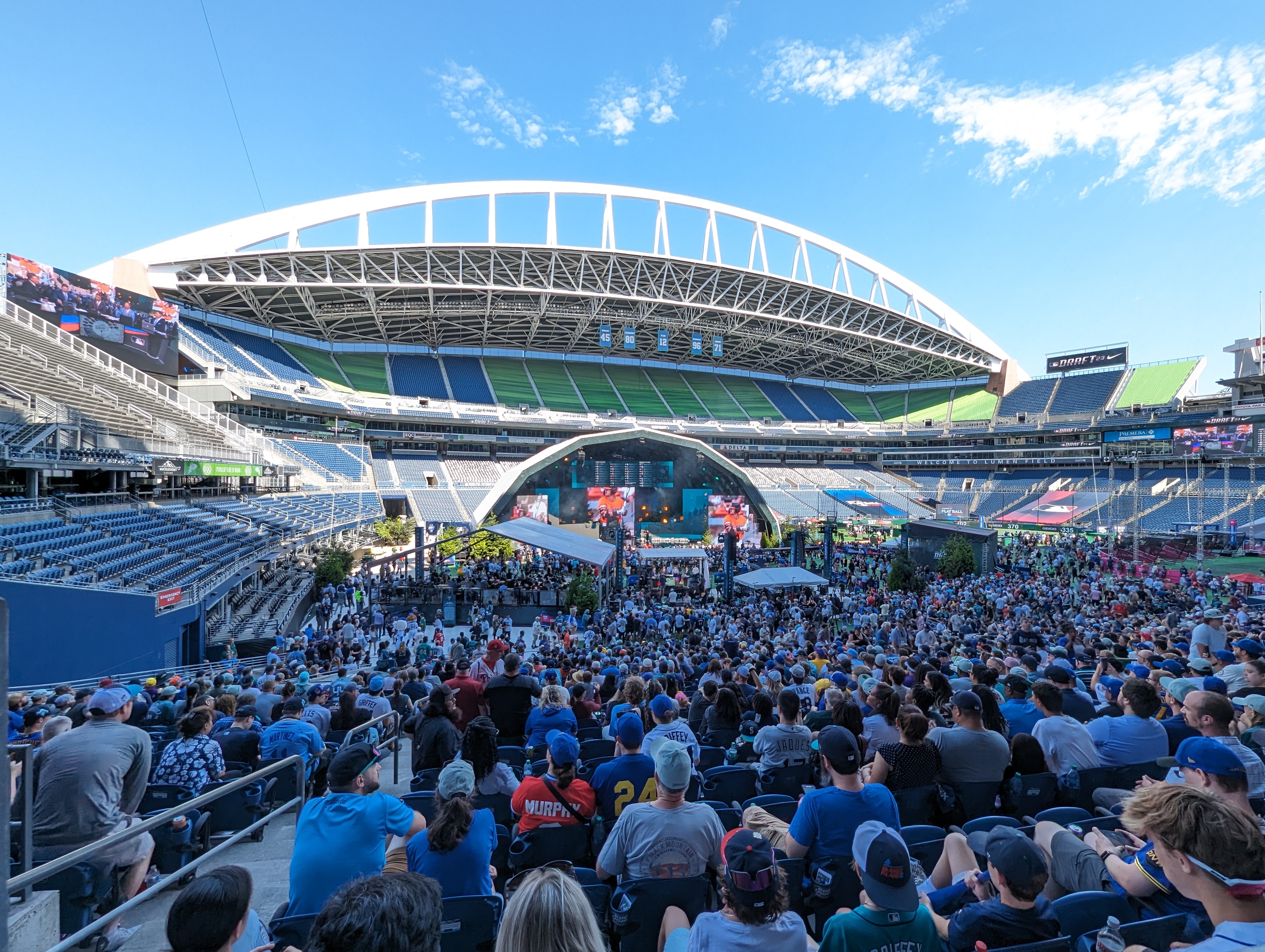 Spectators watch the MLB Draft from stadium seats with a temporary stage on the field.