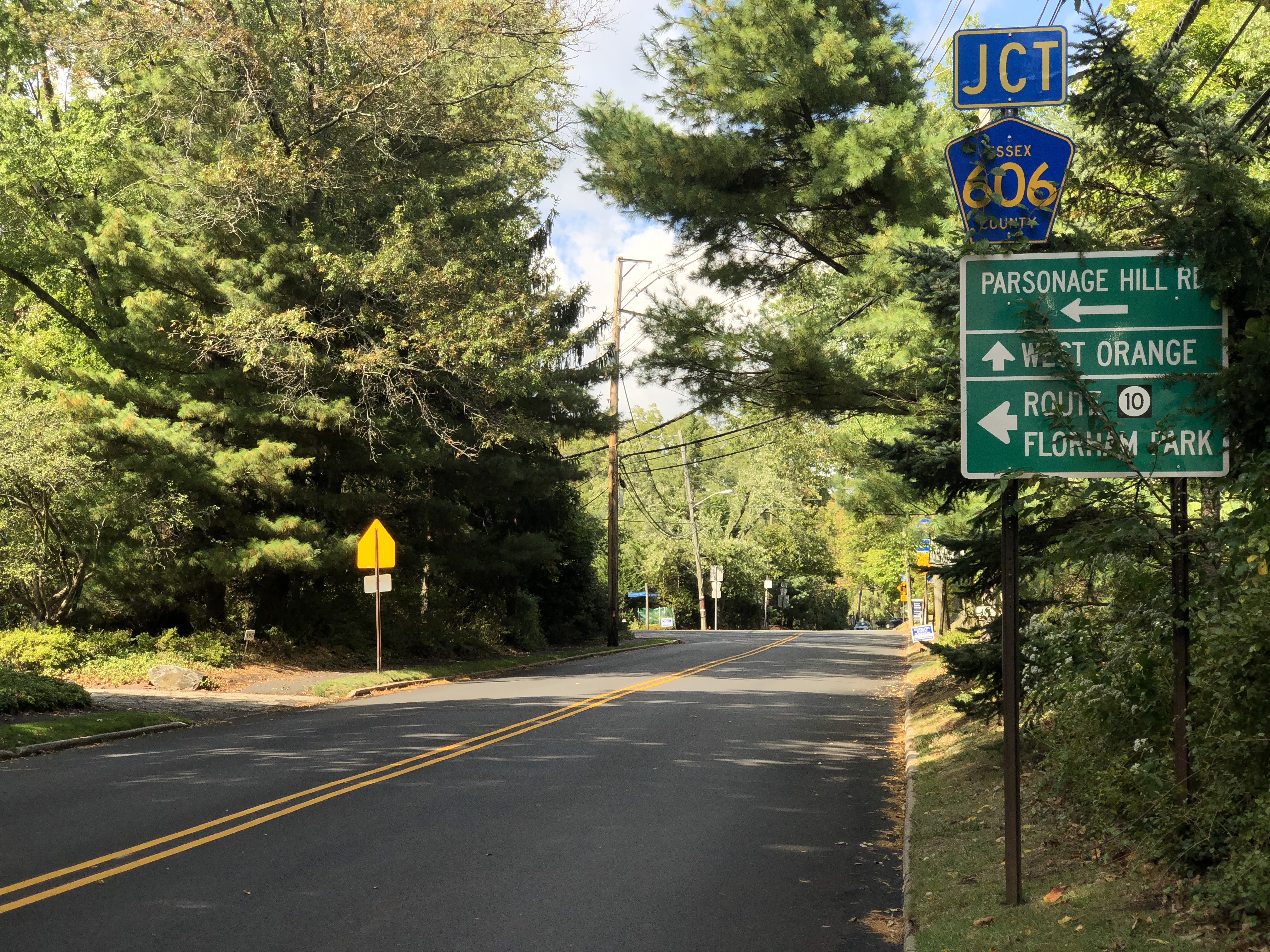 Tree-lined two-lane road with road signs at an intersection on an autumn day.