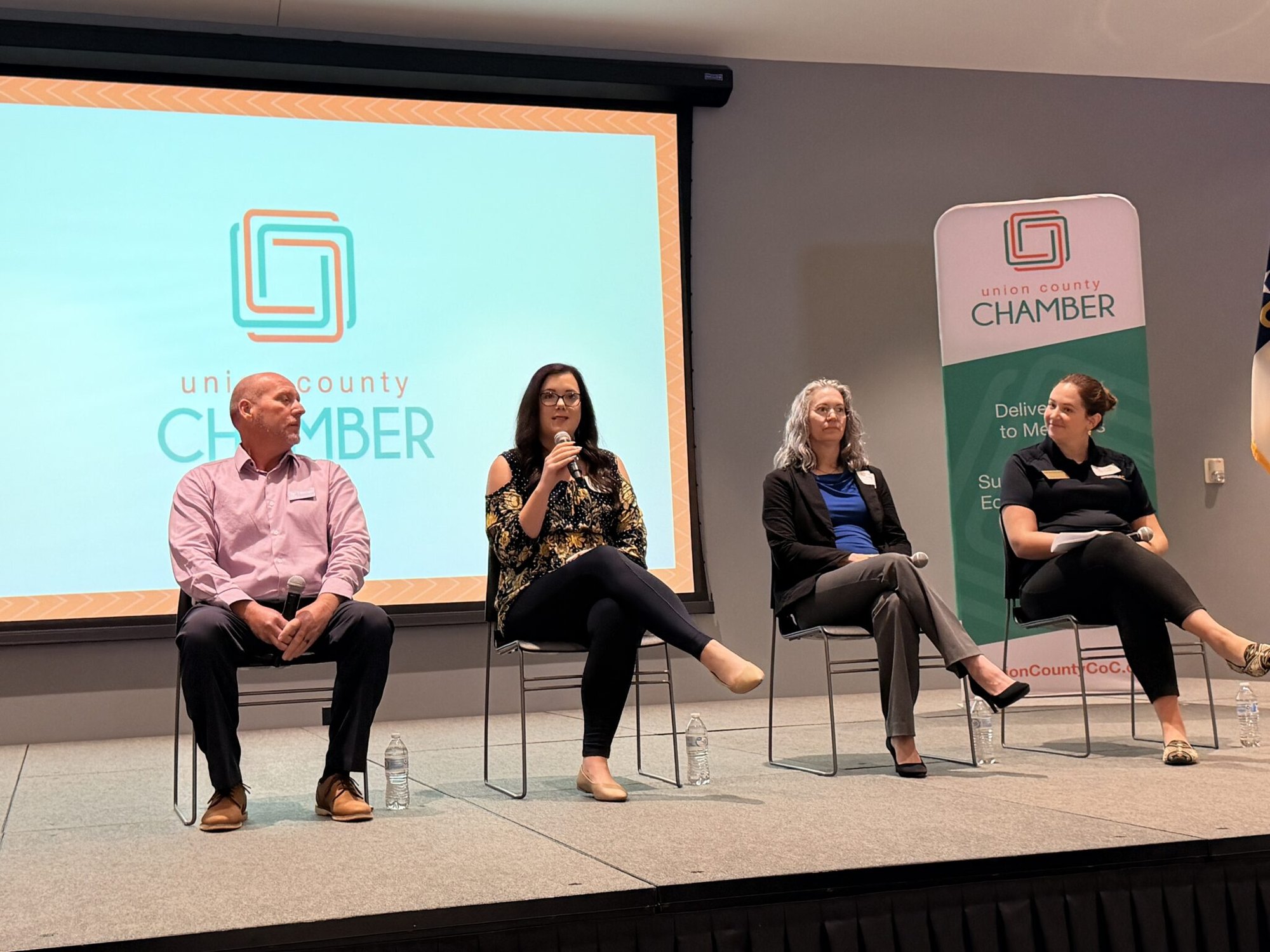 Four panelists seated on a stage at a conference, one holding a microphone.