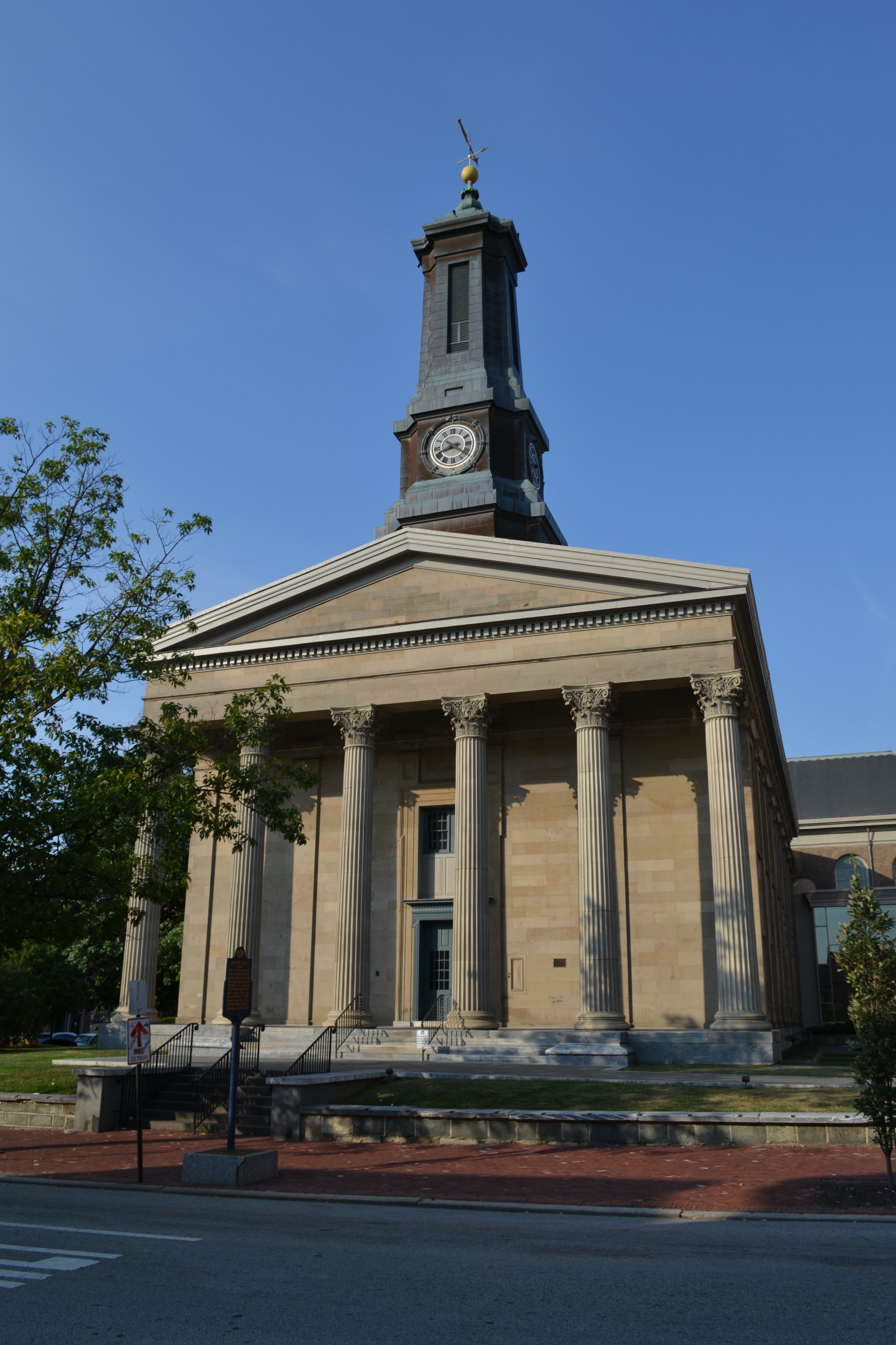 Neoclassical stone courthouse with tall columns and a clock tower under blue sky.