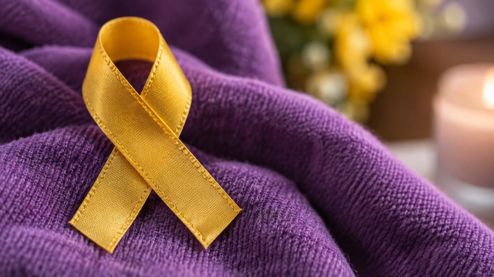 Gold awareness ribbon resting on purple fabric background.