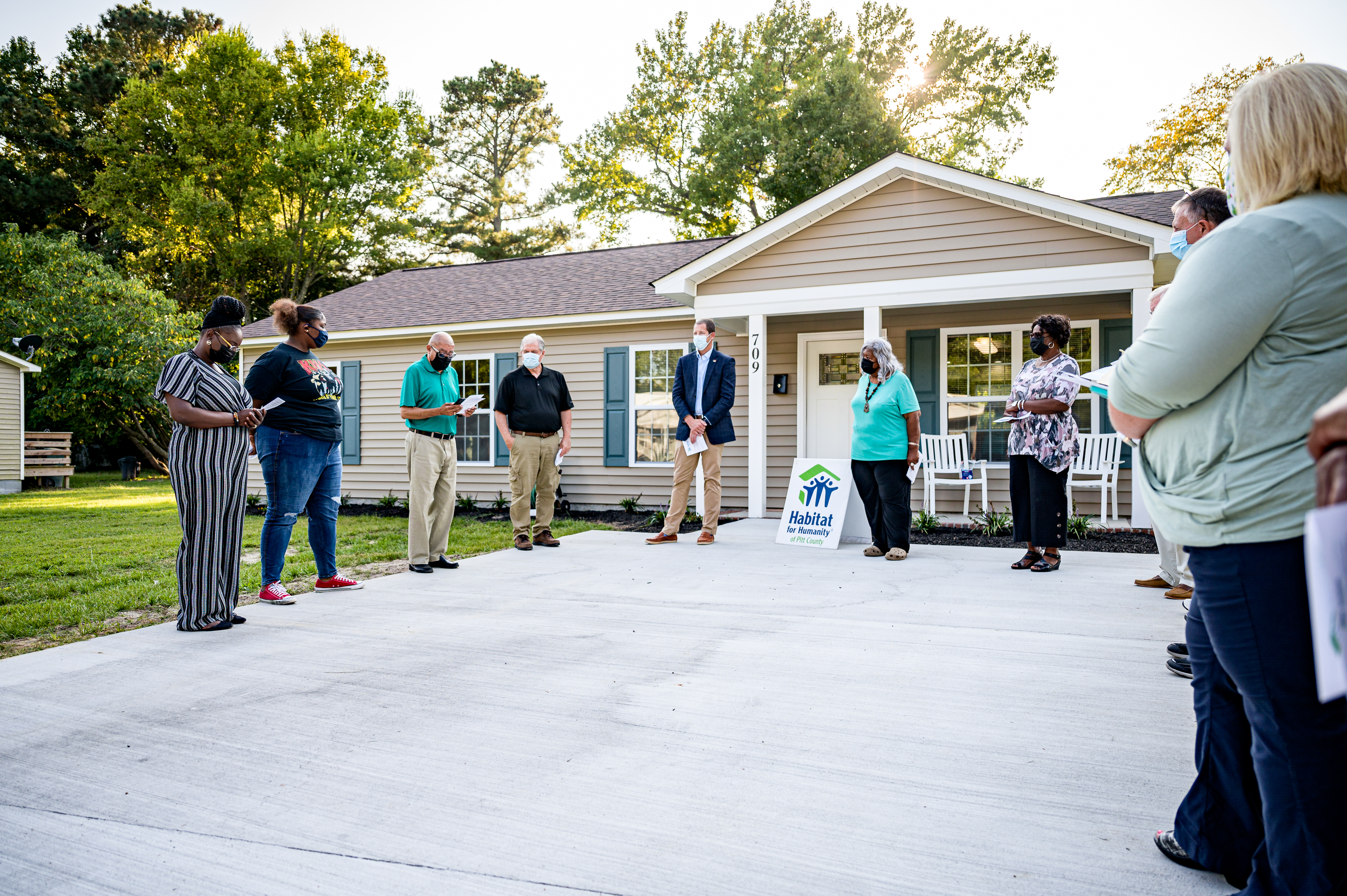 Group of people gathered on a driveway in front of a newly built home with a Habitat for Humanity sign.