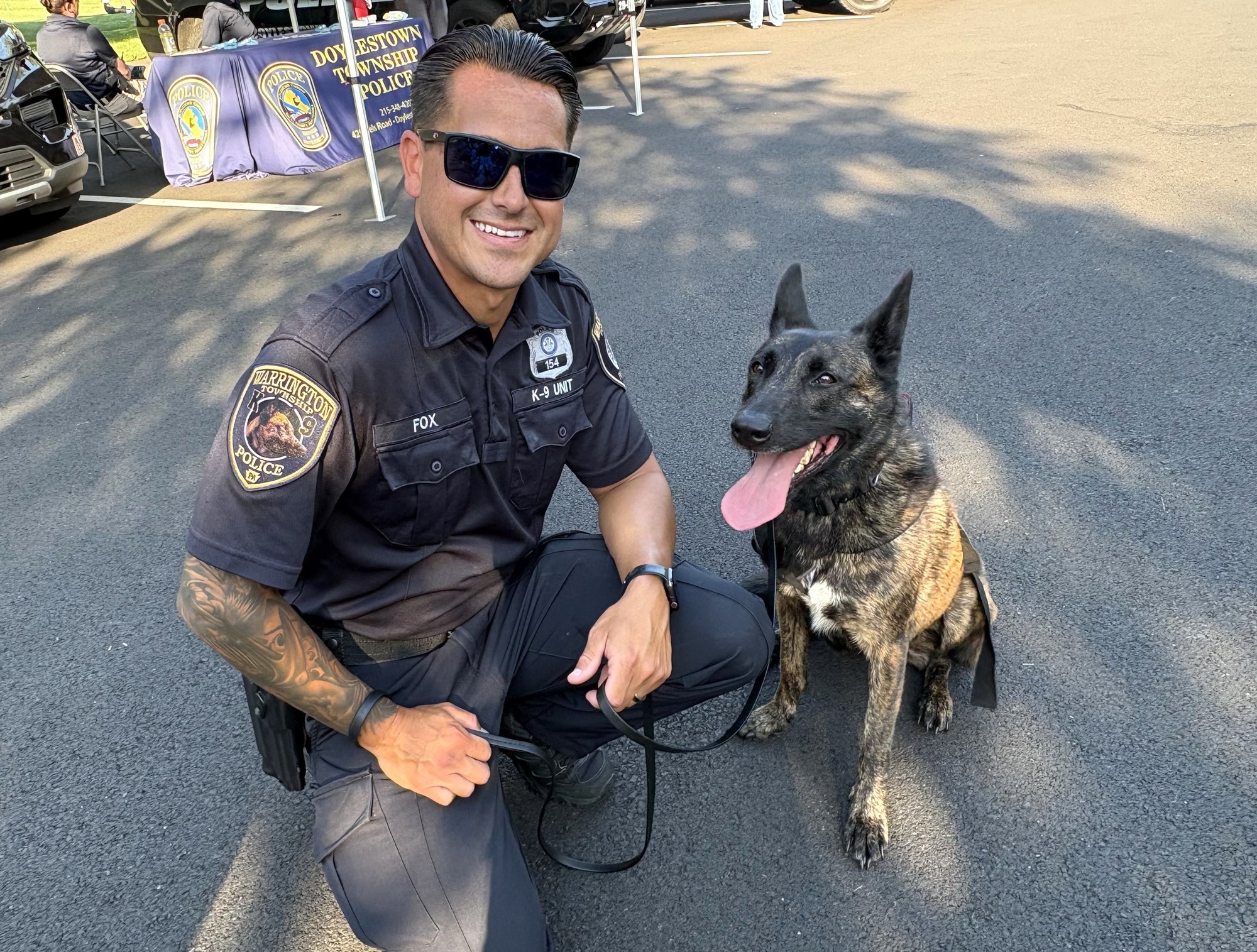 A uniformed officer crouches beside a K-9 dog at an outdoor community event.