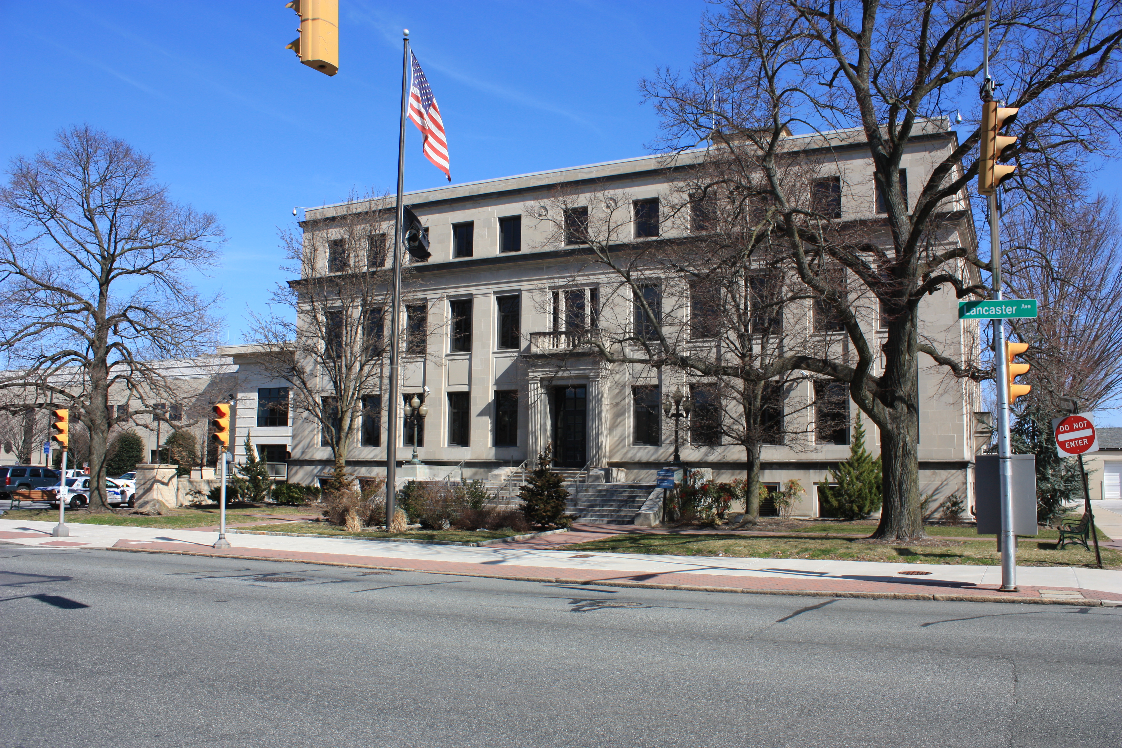 Neoclassical stone government building with an American flag and bare trees in front.