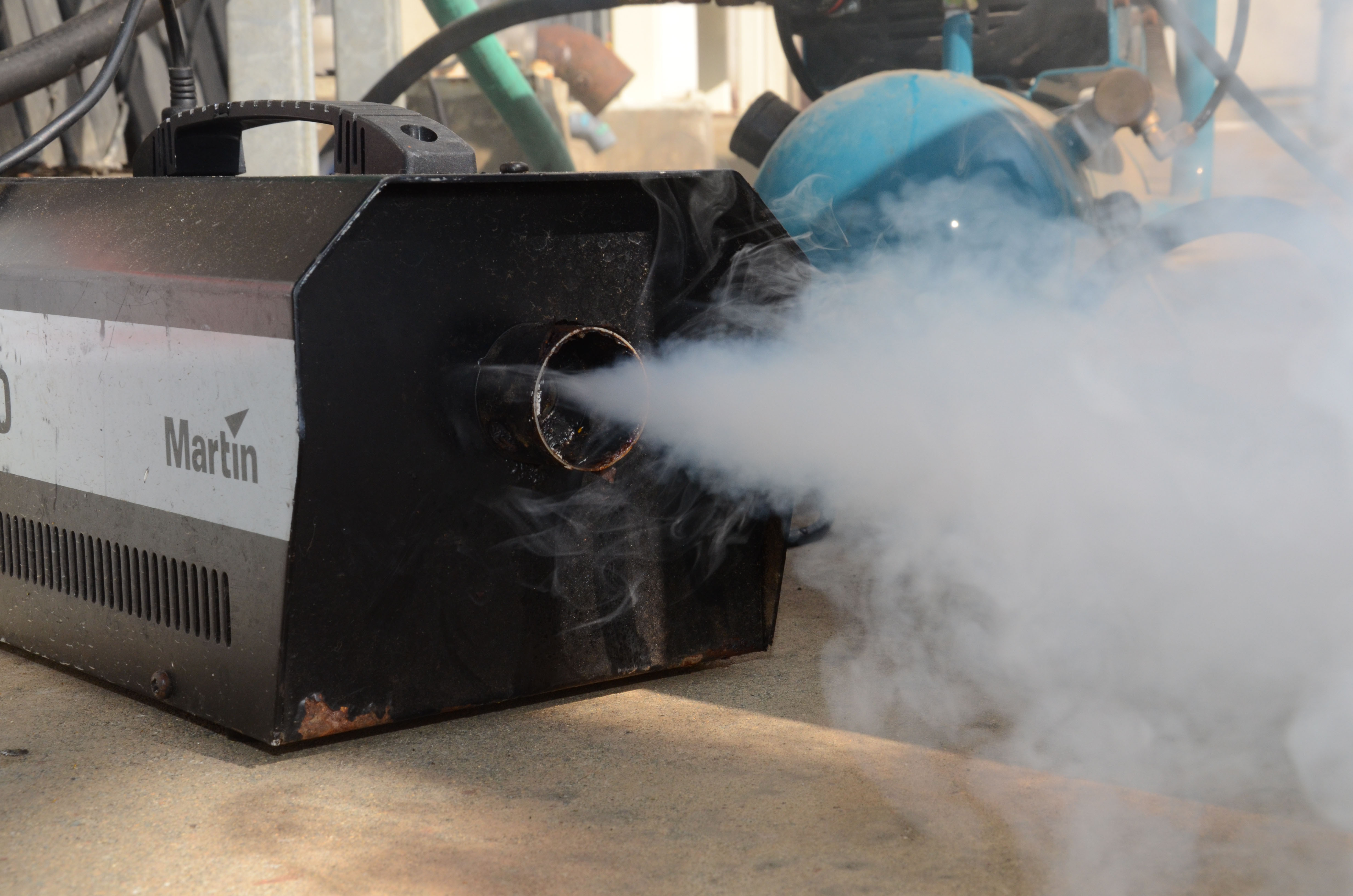 Smoke machine emitting a white plume outdoors at a large industrial campus.
