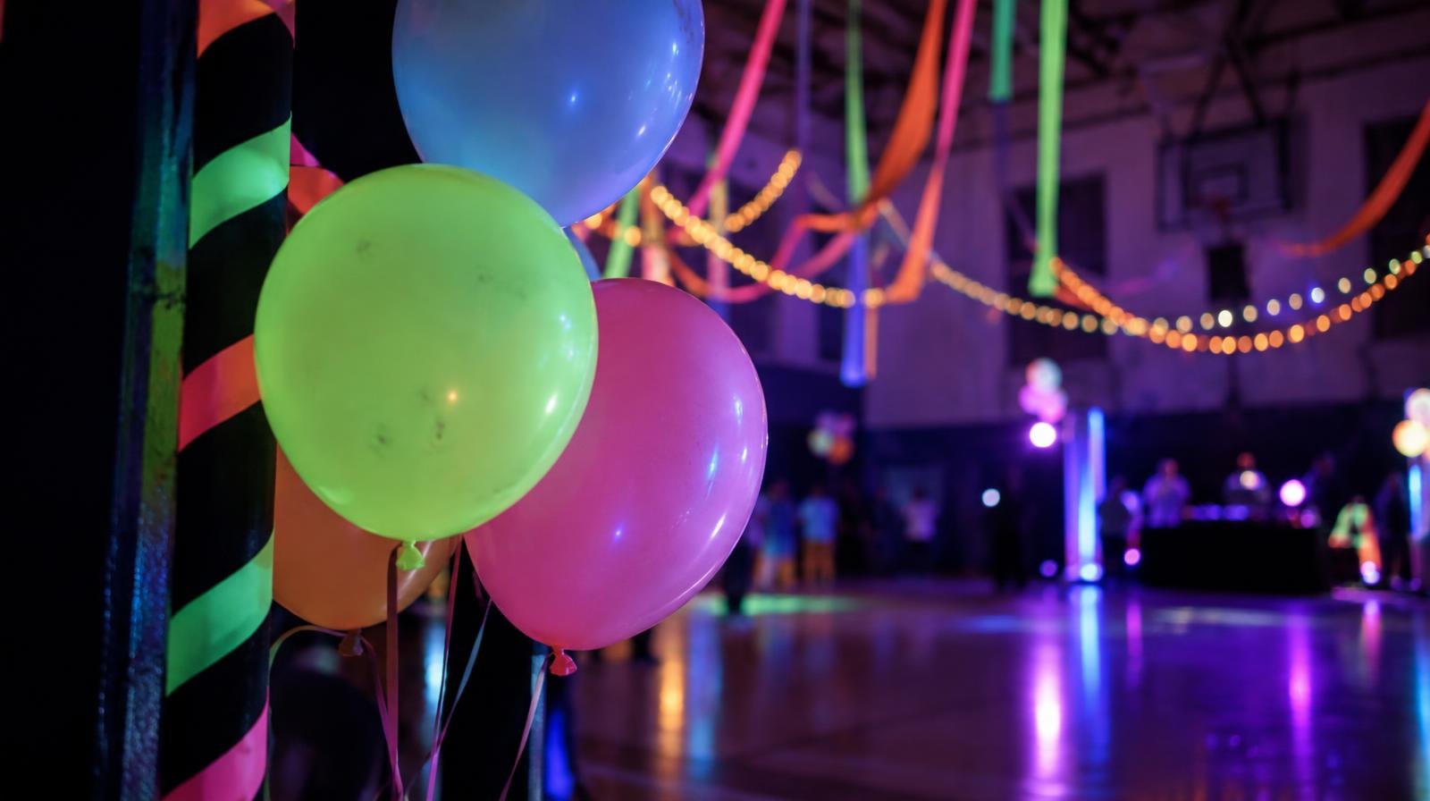 Colorful neon streamers and decorations glowing in a dark gymnasium.