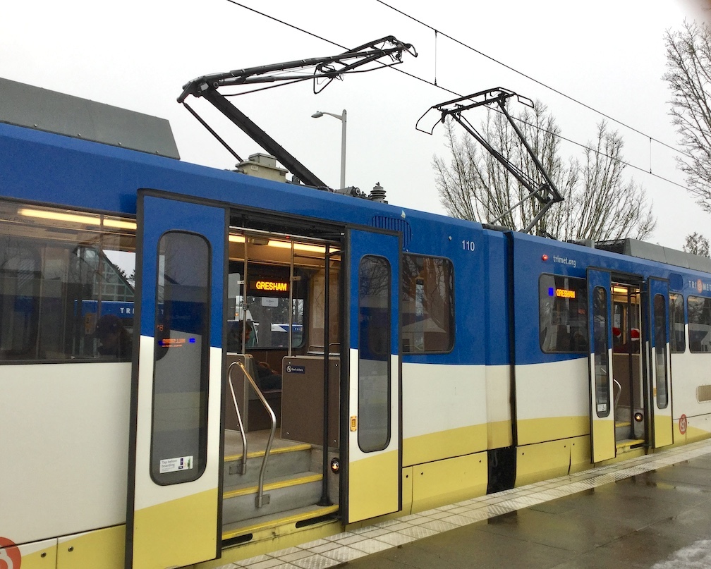 A blue and white TriMet MAX light rail car with open doors stopped at a station platform.