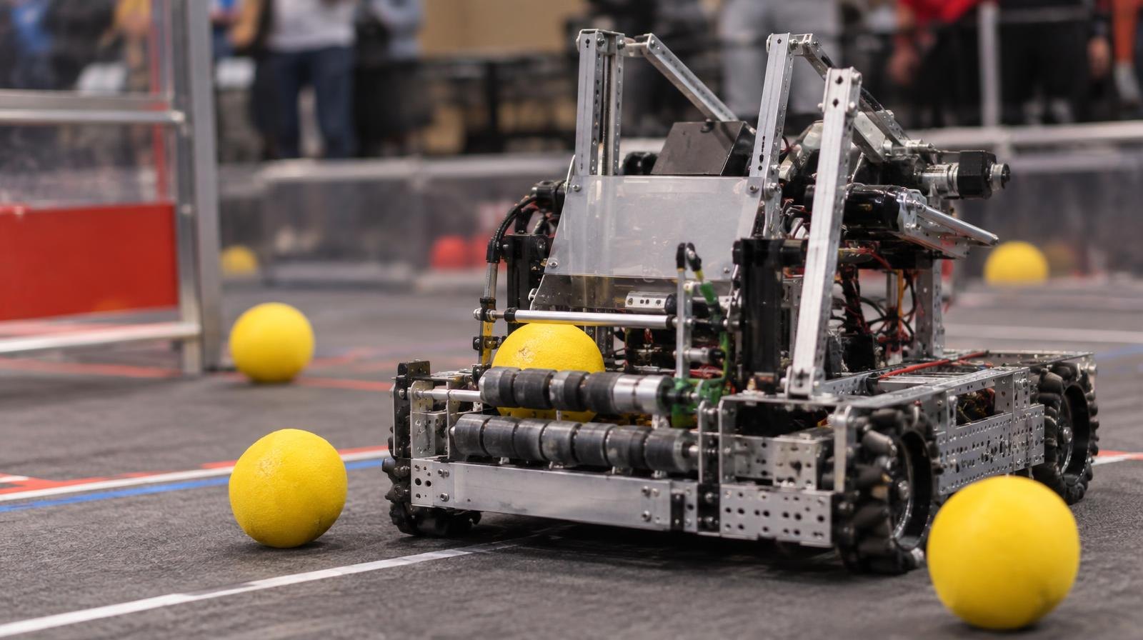 A student-built competition robot surrounded by yellow balls on a marked arena floor.