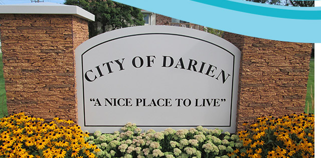 Stone monument sign reading City of Darien with yellow and white flowers in front.