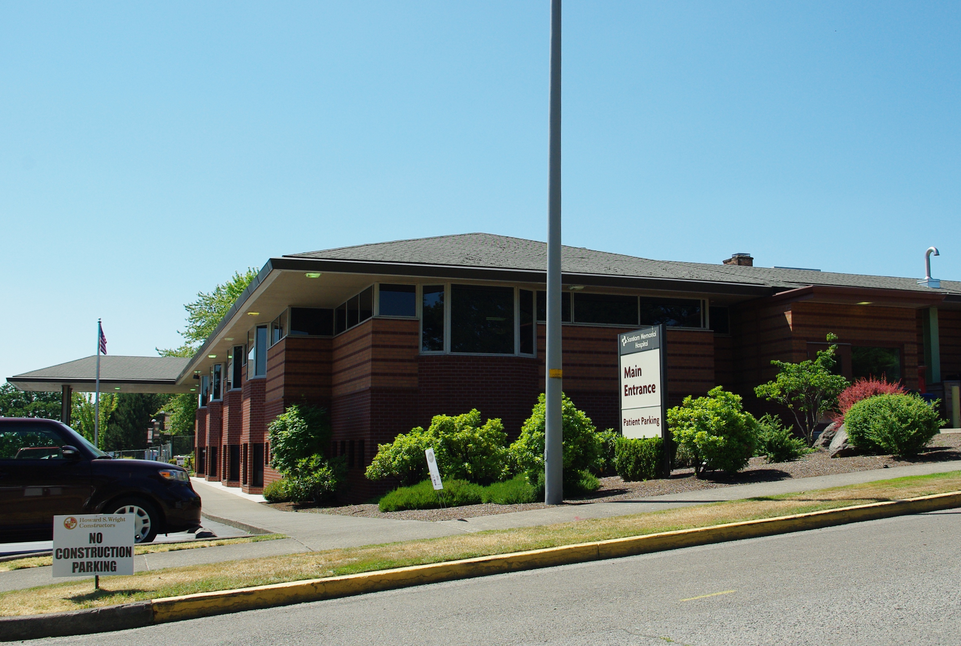 Single-story brown brick hospital building with flagpole and landscaped entrance.