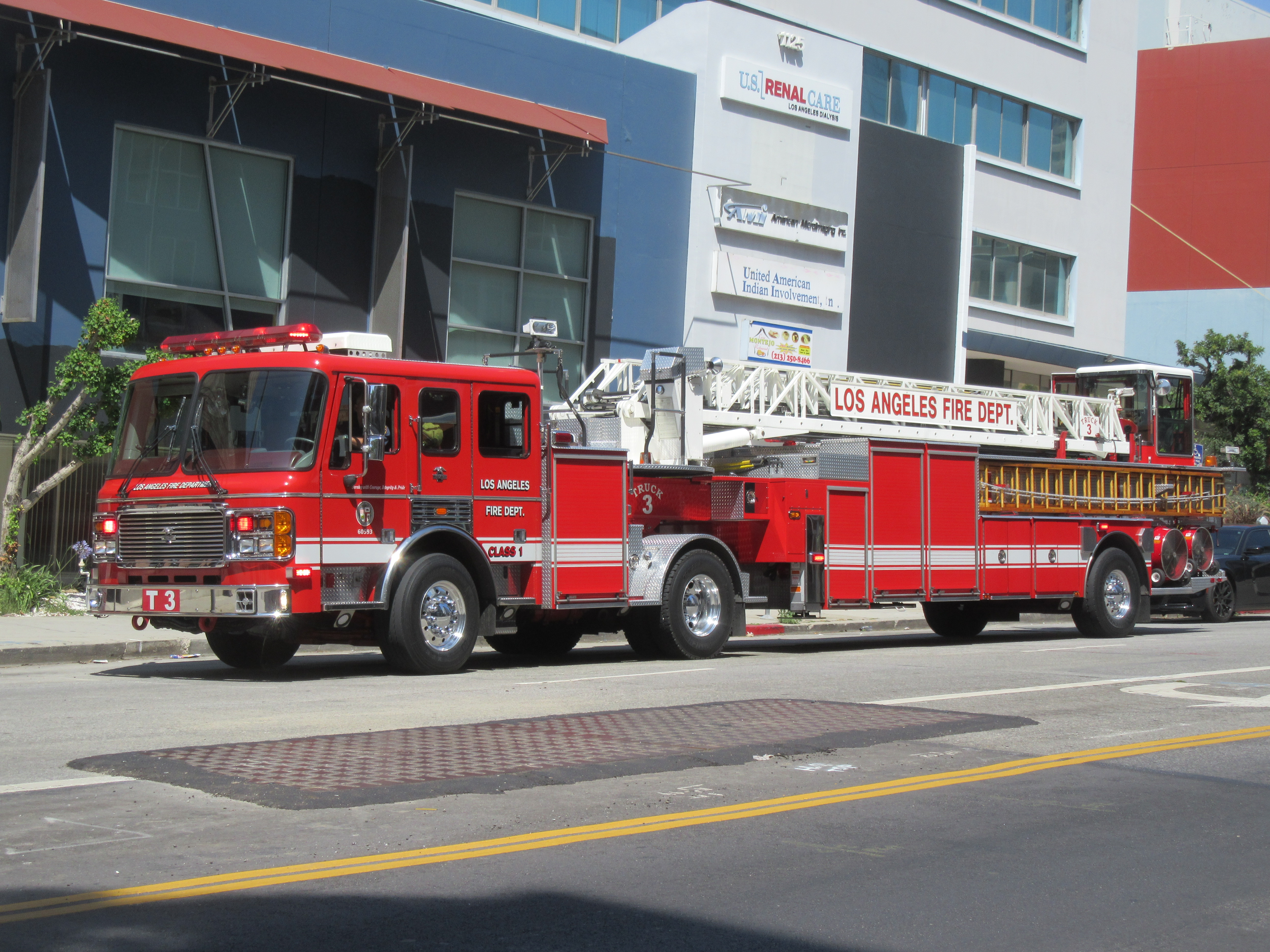 Red Los Angeles Fire Department tiller aerial ladder truck parked on a city street.