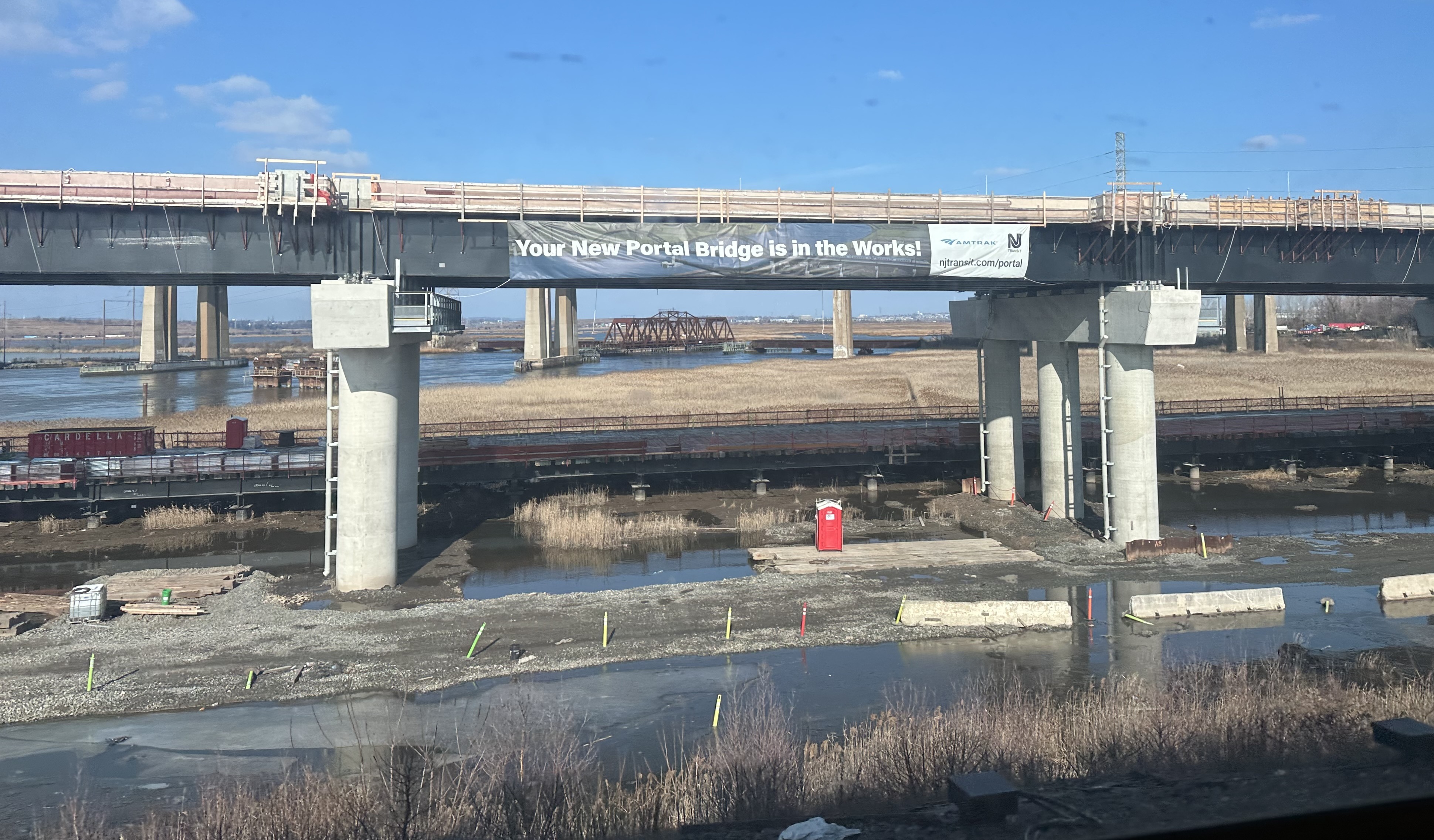 New rail bridge under construction over a river, with a project banner visible.